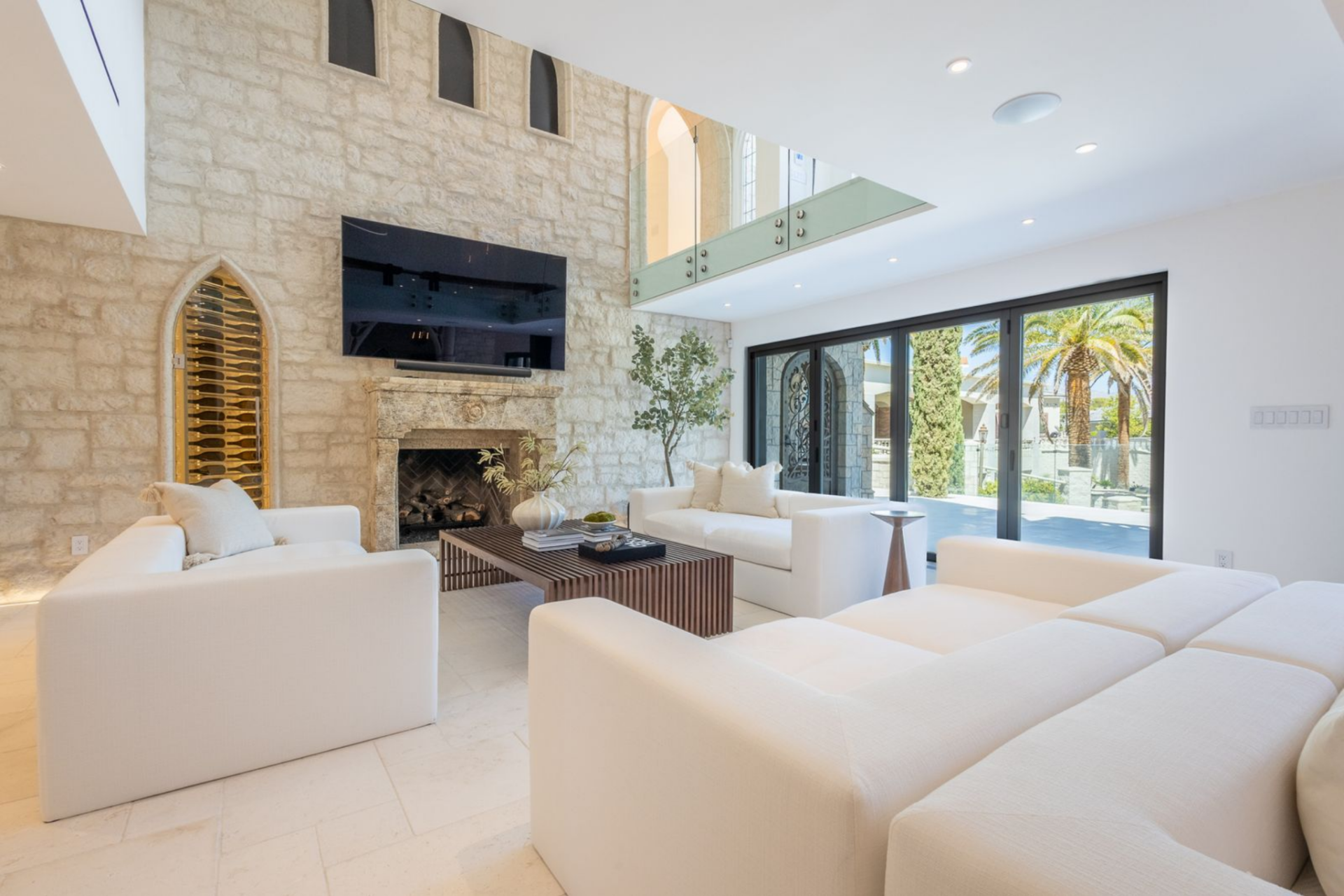 At the center of the room, a carved stone fireplace anchors one wall, with a television mounted above and a pointed arched wine display tucked beside it as a subtle nod to the Gothic detailing seen outside.