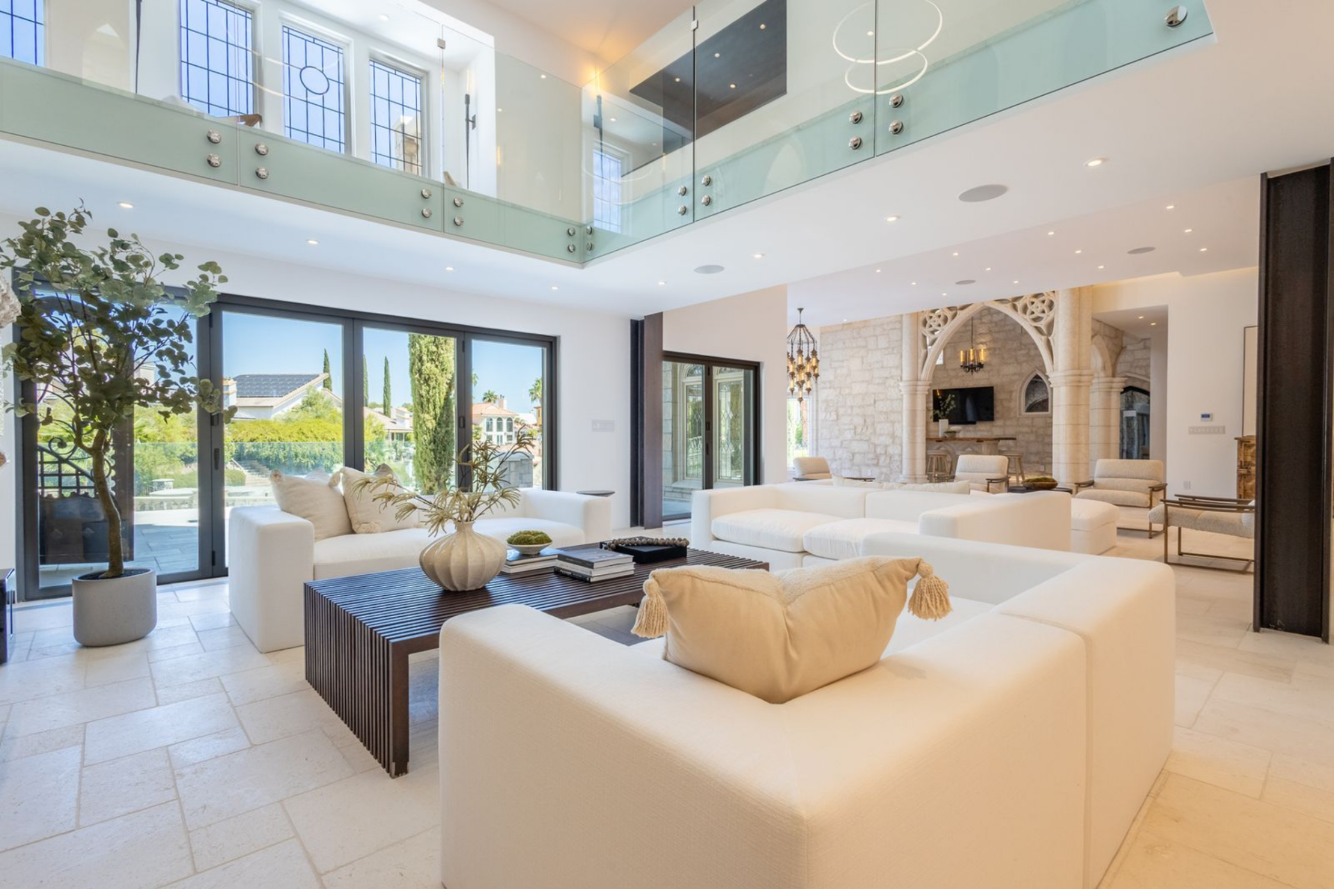 Across the back of the room, wide sliding glass doors open the space directly to the terrace, bringing in daylight and views of the exterior architecture, palms, and surrounding hardscape.