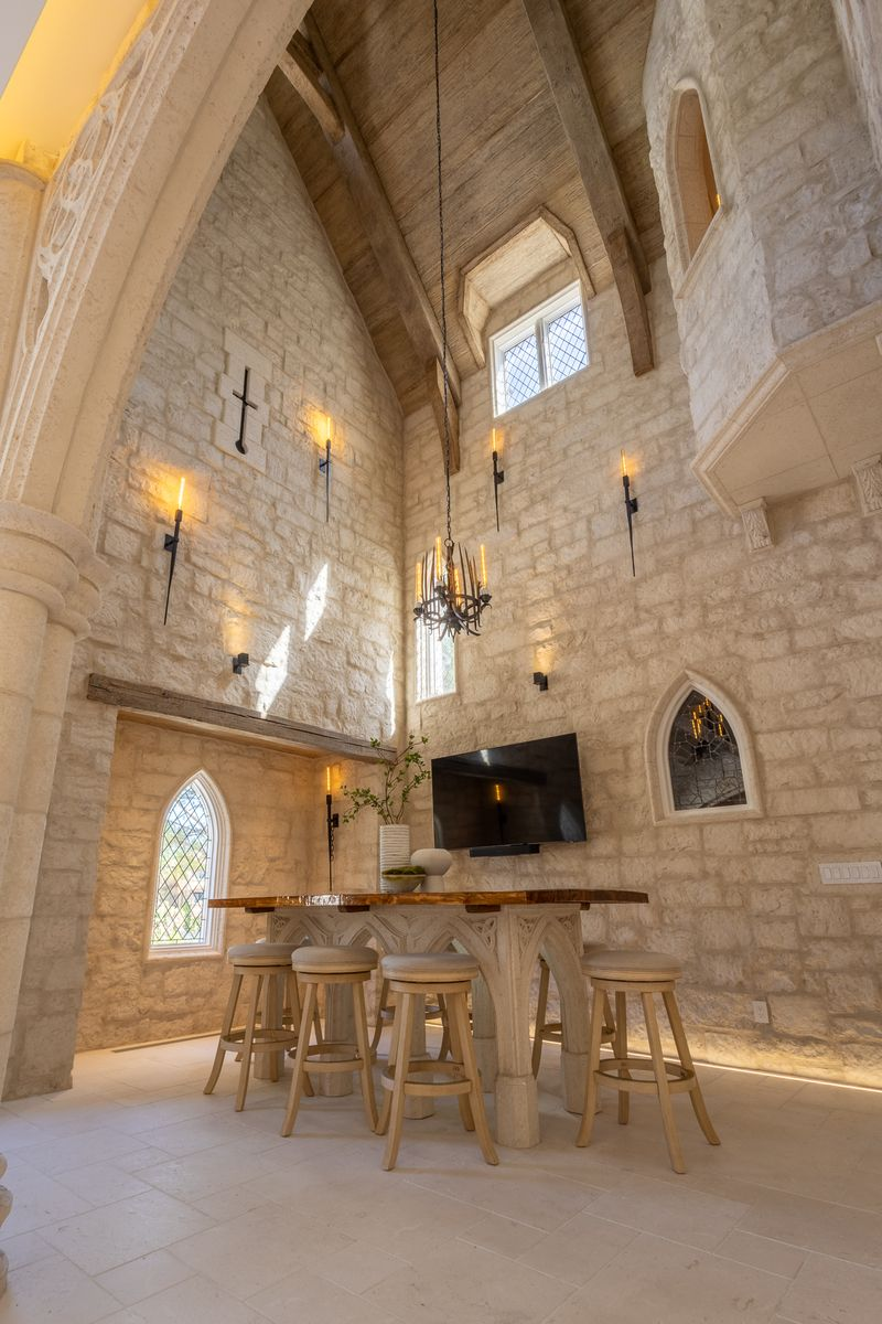 The table itself continues the Gothic design of the house with a carved trestle-style base that mirrors the pointed arches in the surrounding windows and wall openings.