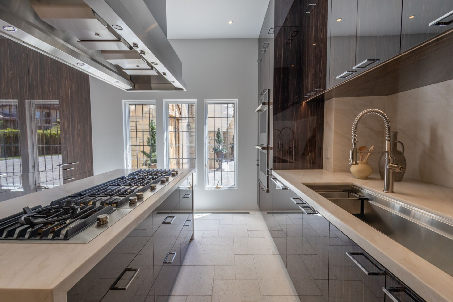 Along the perimeter, the counters continue beneath the reflective cabinetry, with a second sink, built-in appliances, and storage arranged in crisp linear lines.