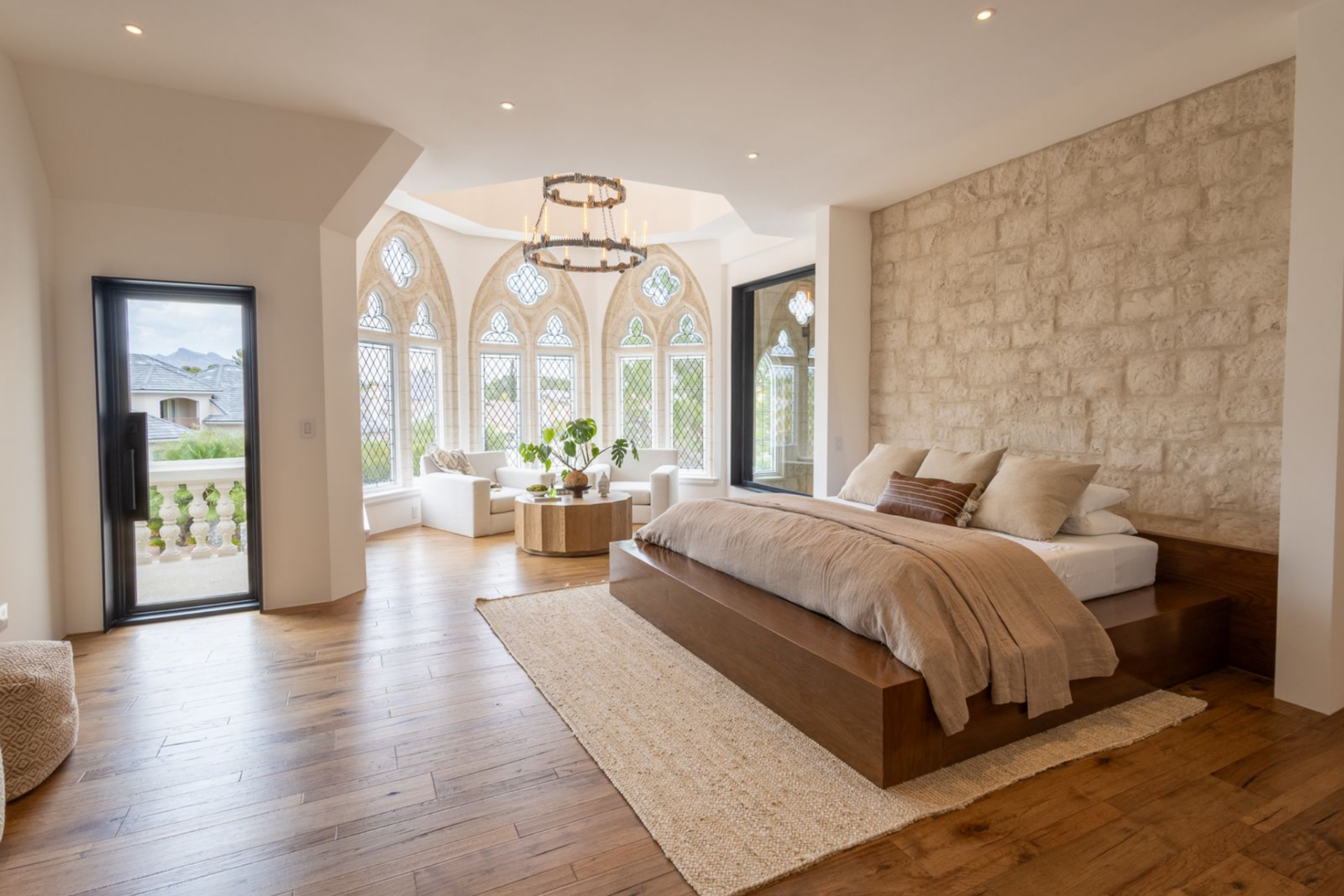 The bedroom opens across warm wood floors and white walls, with a low platform bed set against a full limestone feature wall.