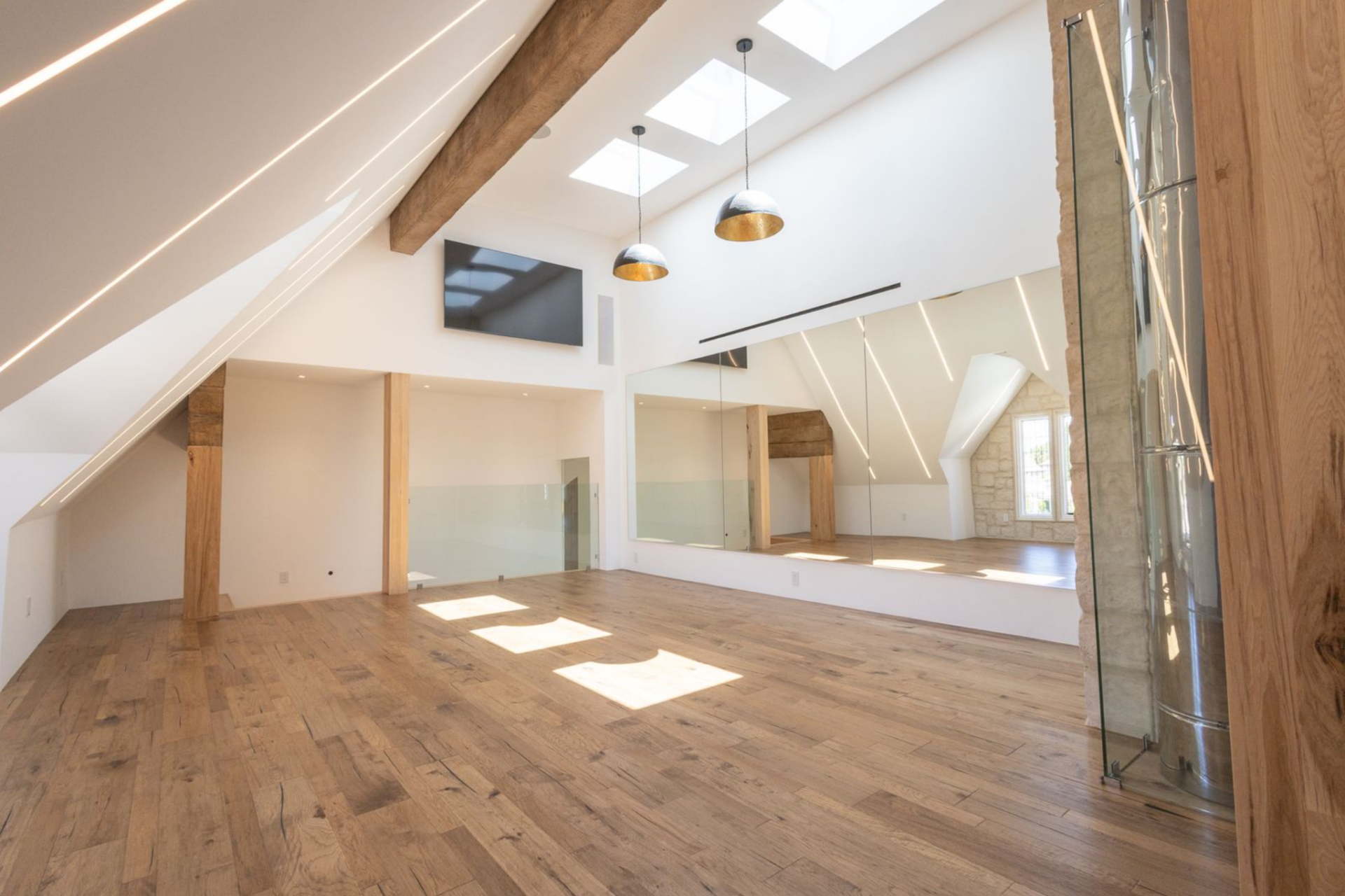 One wall is lined with oversized mirrors, which expands the sense of volume and reflects the sharp ceiling lines across the room, while a mounted screen and suspended dome lights make the space perfect as a training studio.
