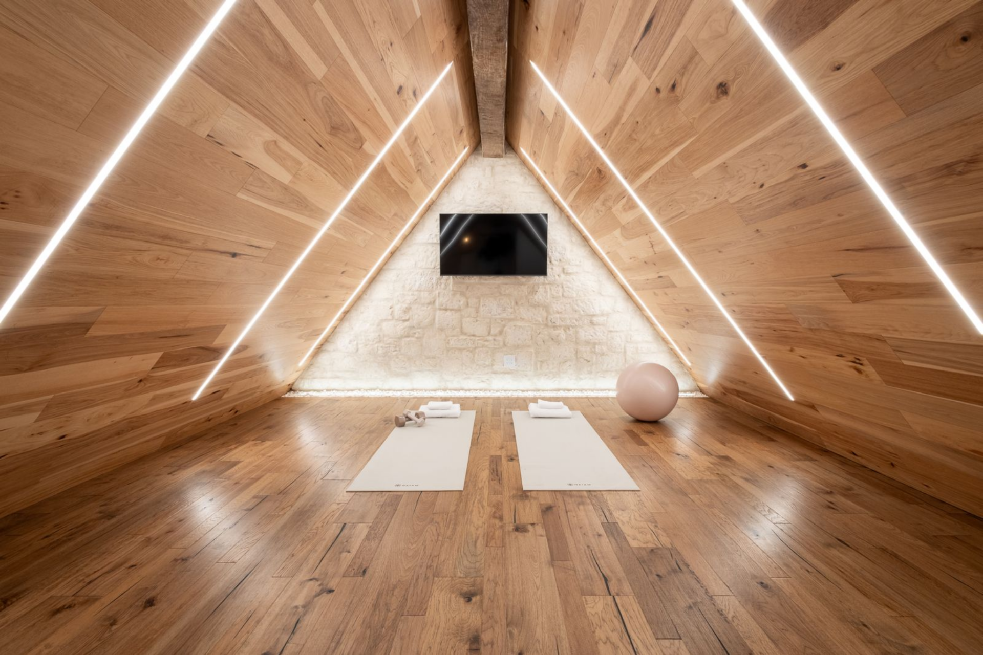 Here, the sloped wood ceilings drop low on both sides and are traced with linear lighting. A limestone wall serves as the TV background, while mats and light weights make it perfect for yoga or pilates.