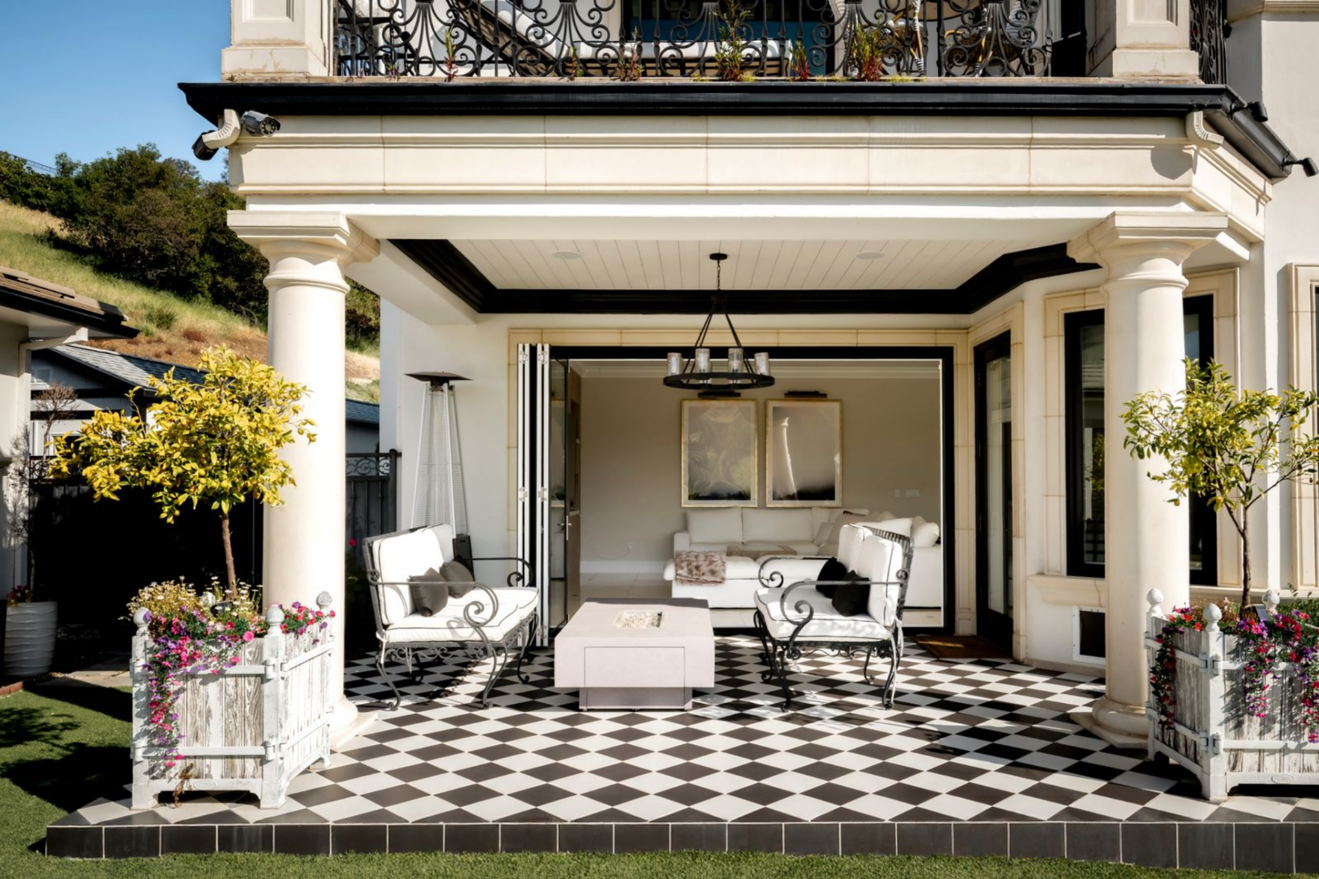 Framed by columns and soft landscaping, the space is arranged with wrought-iron seating around a gas firepit, creating a shaded space that connects directly back to the living room.