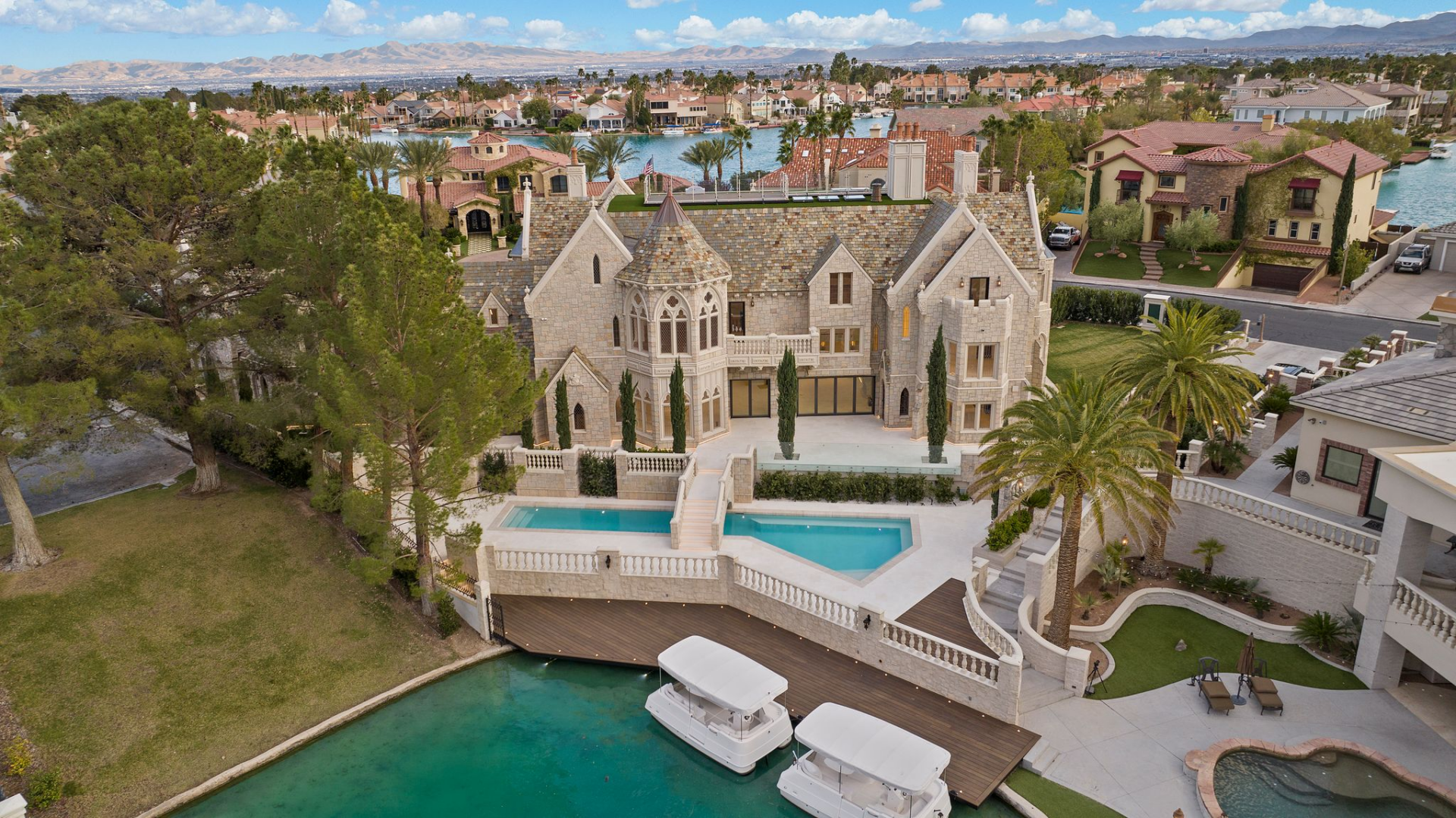 Down below, the pool area is arranged on a lower terrace at the back of the house, where the water is framed by balustrades, broad staircases, and stone surfaces that match the rest of the exterior.