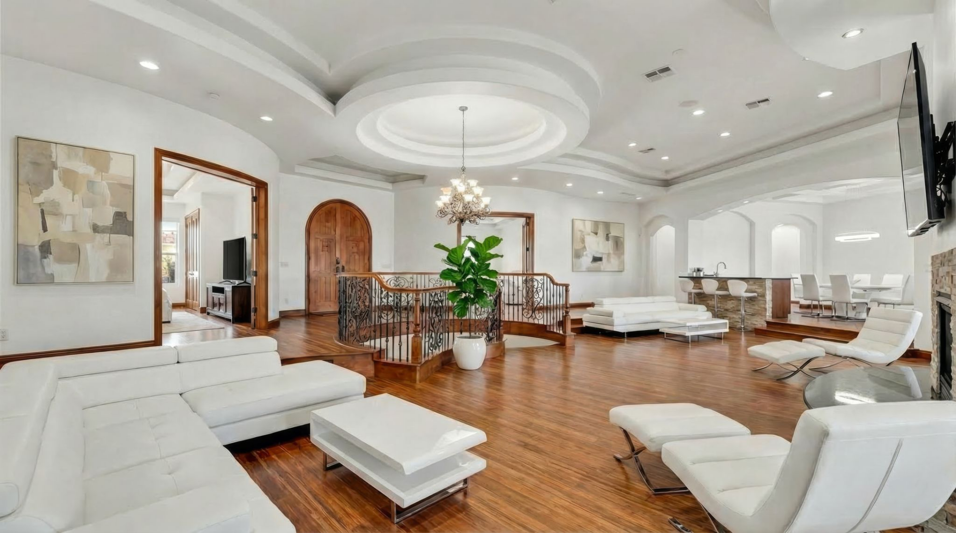 The foyer has an expansive, open-plan with curved ceiling details, wide wood floors, and a staircase wrapped in decorative iron railing leading to the basement.