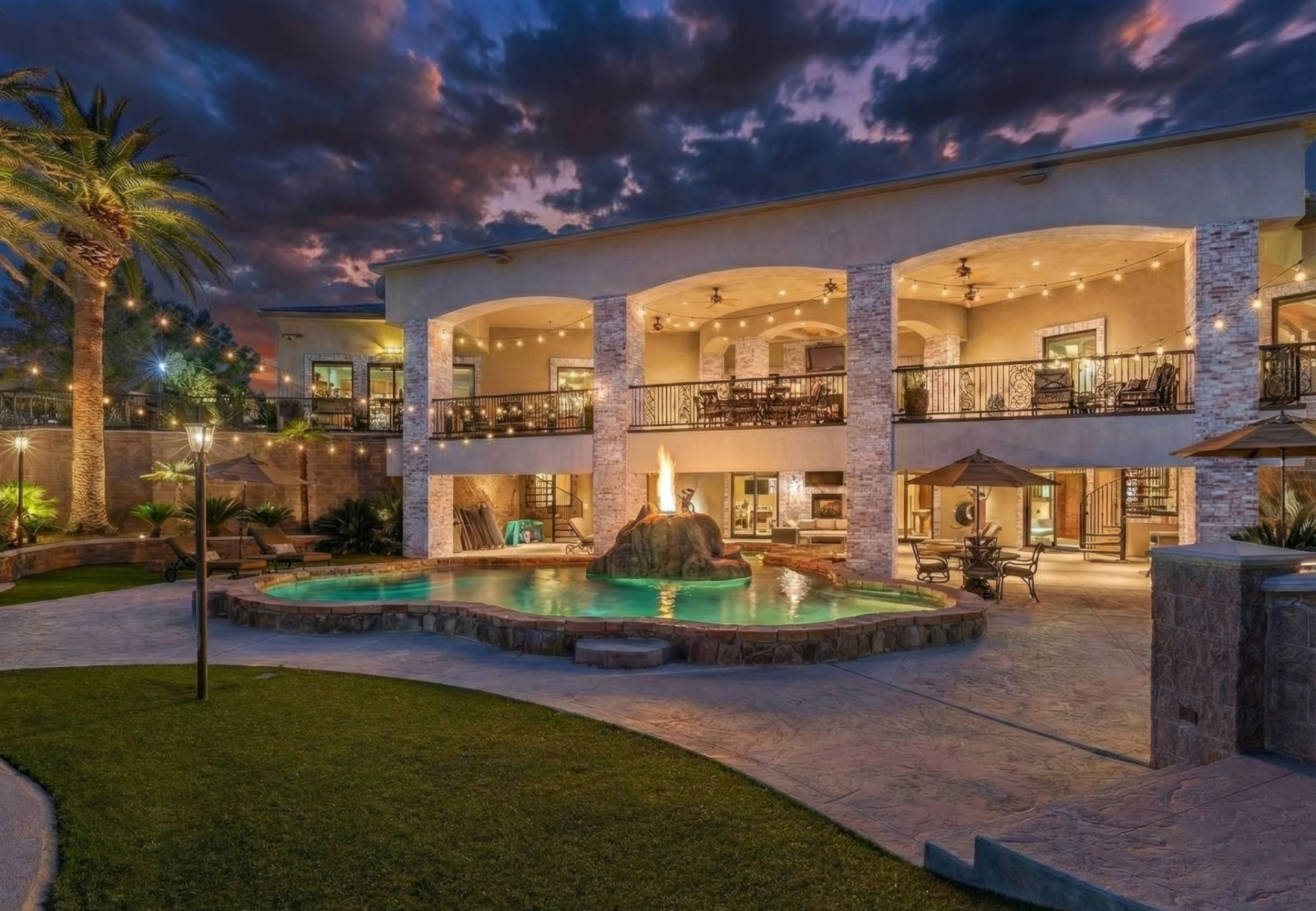 Outside, the backyard begins with covered terraces stretching the width of the house, followed by a freeform pool in the middle of the space, all surrounded by palm trees and string lights.