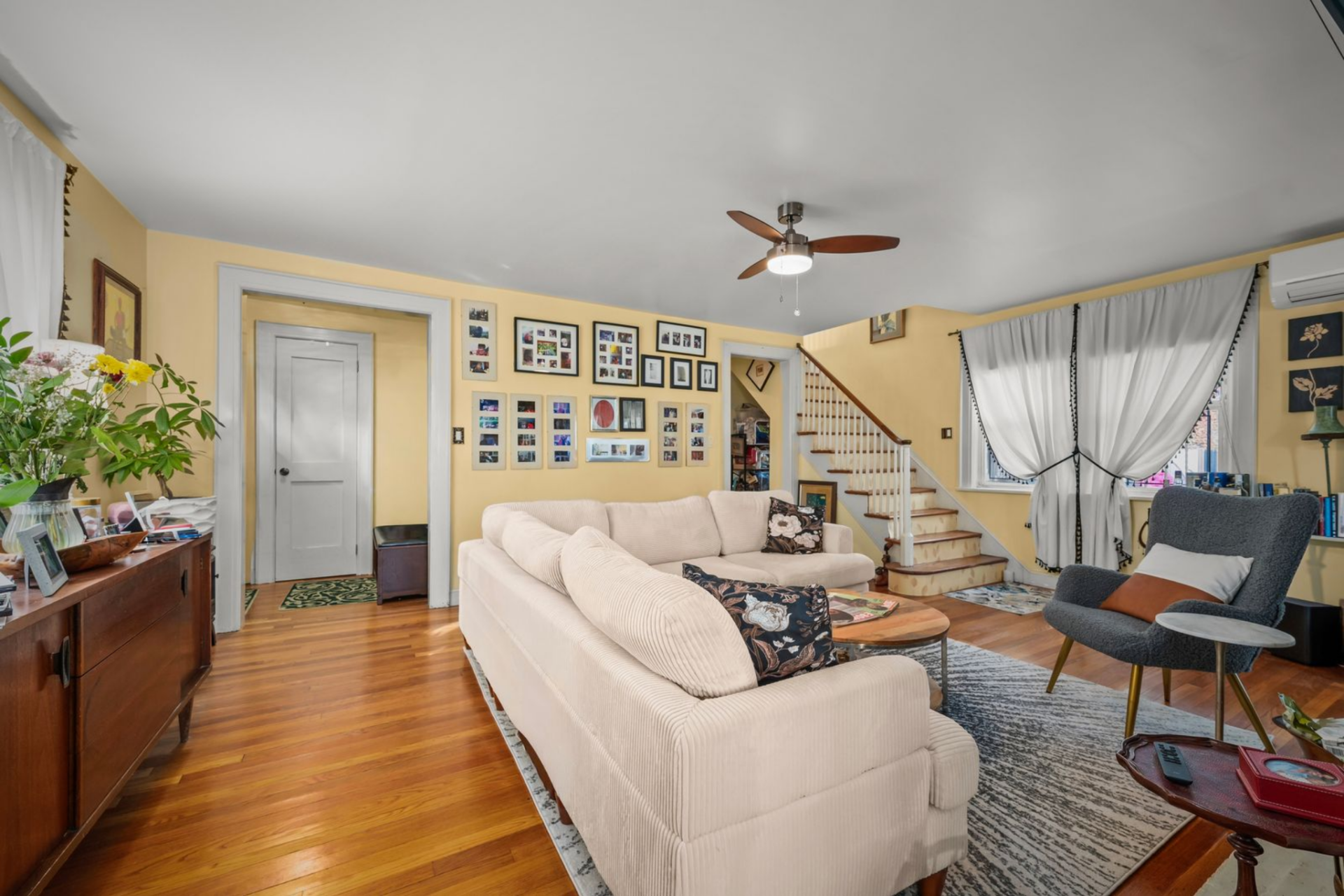 Family photos line one wall near the staircase, windows are dressed with soft drapery, and the arched openings on either side of the blue wall keep the space open.
