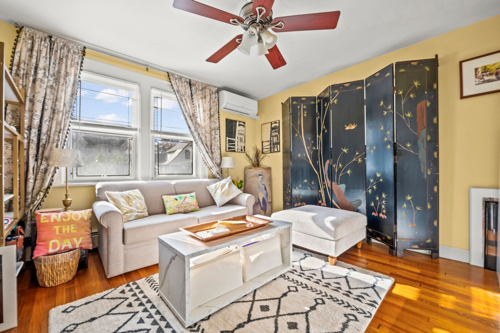 The space is arranged around a sofa and ottoman, while a painted folding screen creates a decorative focal point and the windows bring in daylight over the seating area.