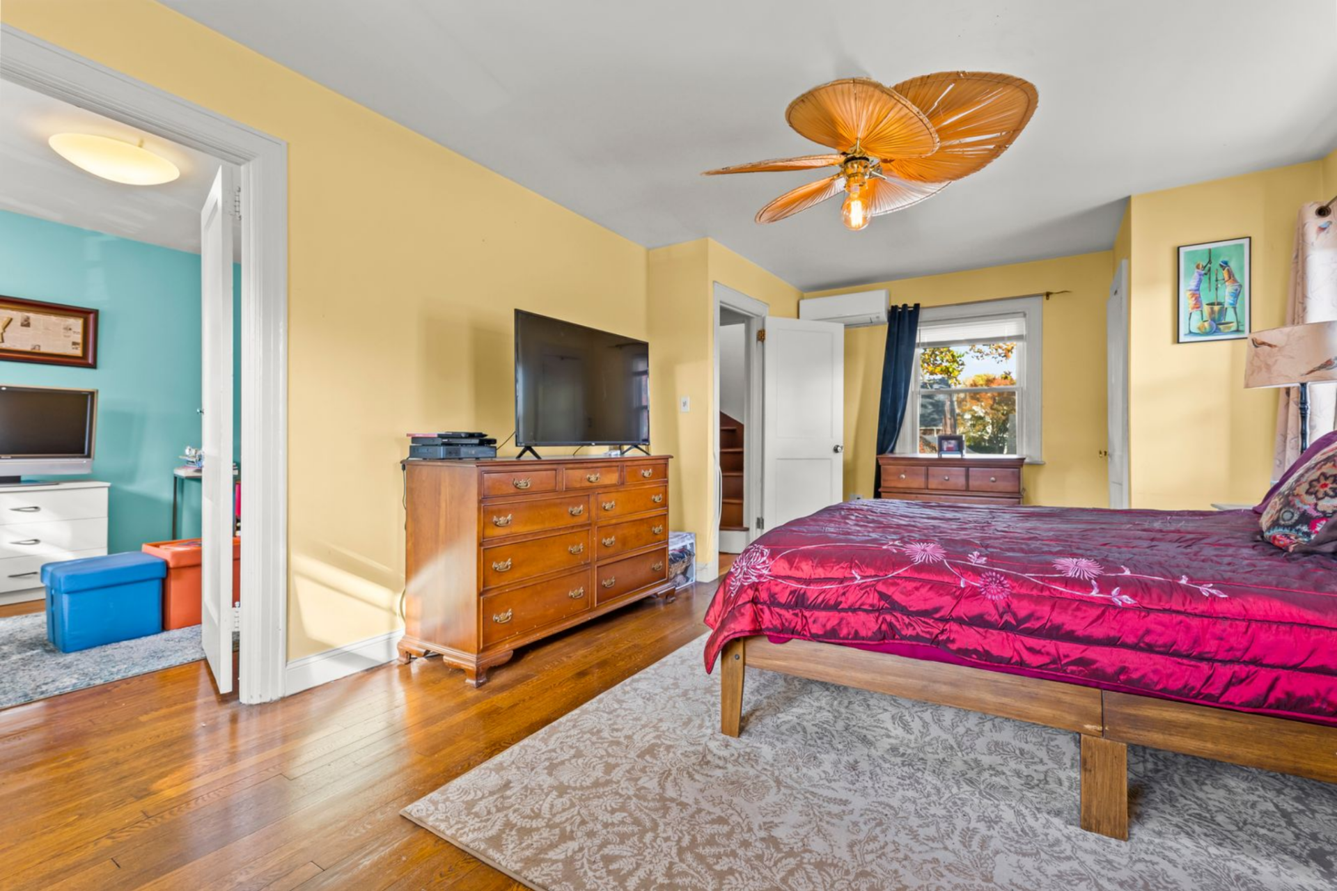 Along the opposite wall, a wood dresser with a mounted TV faces the bed, keeping the circulation path clear between the entry door and the rest of the space.