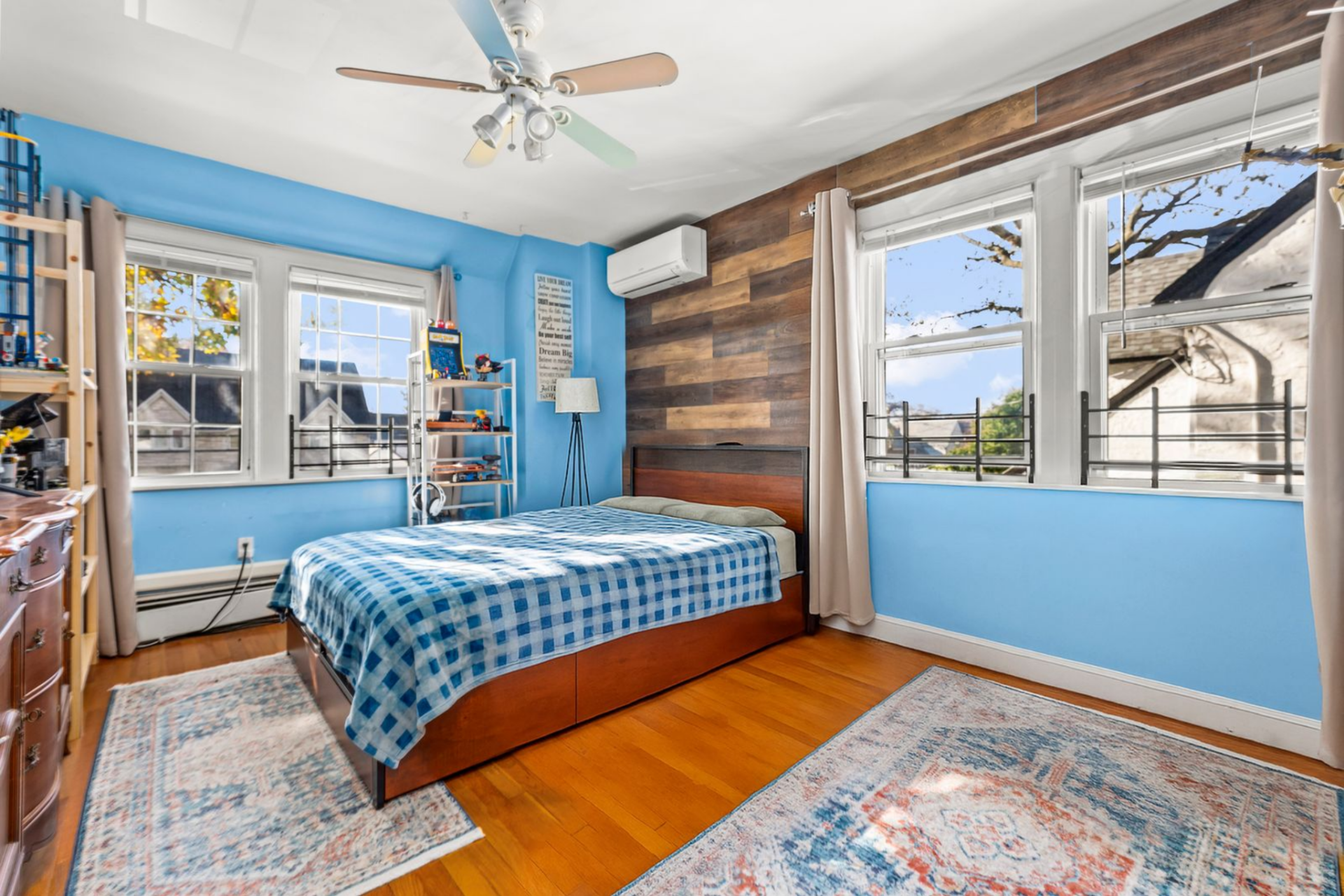 The layout is open with a bed and a mix of shelving and dressers placed along the perimeter, all surrounded by blue-painted walls.