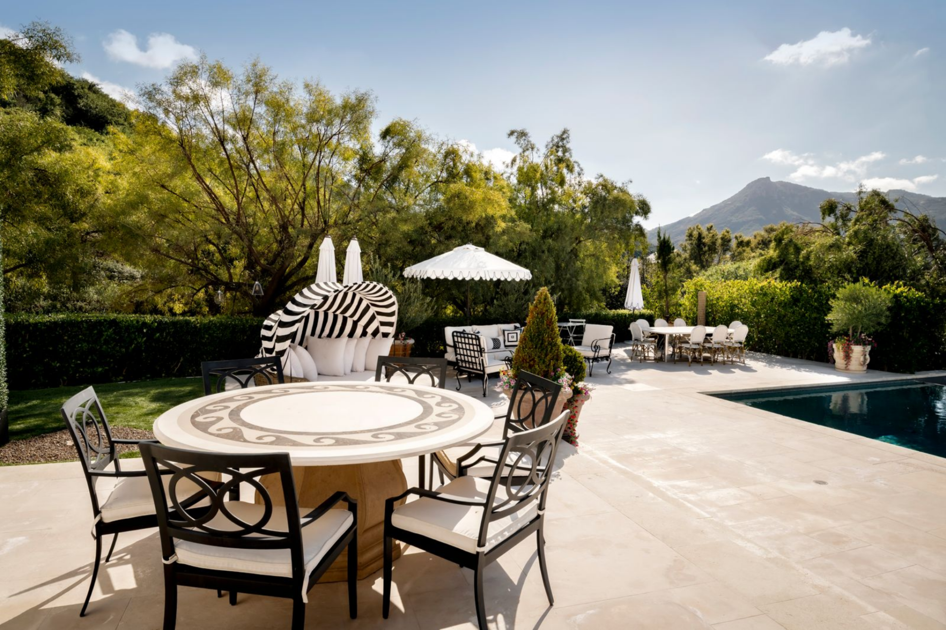 On one side of the pool, several outdoor dining spaces are arranged to accommodate both casual meals and larger gatherings. 