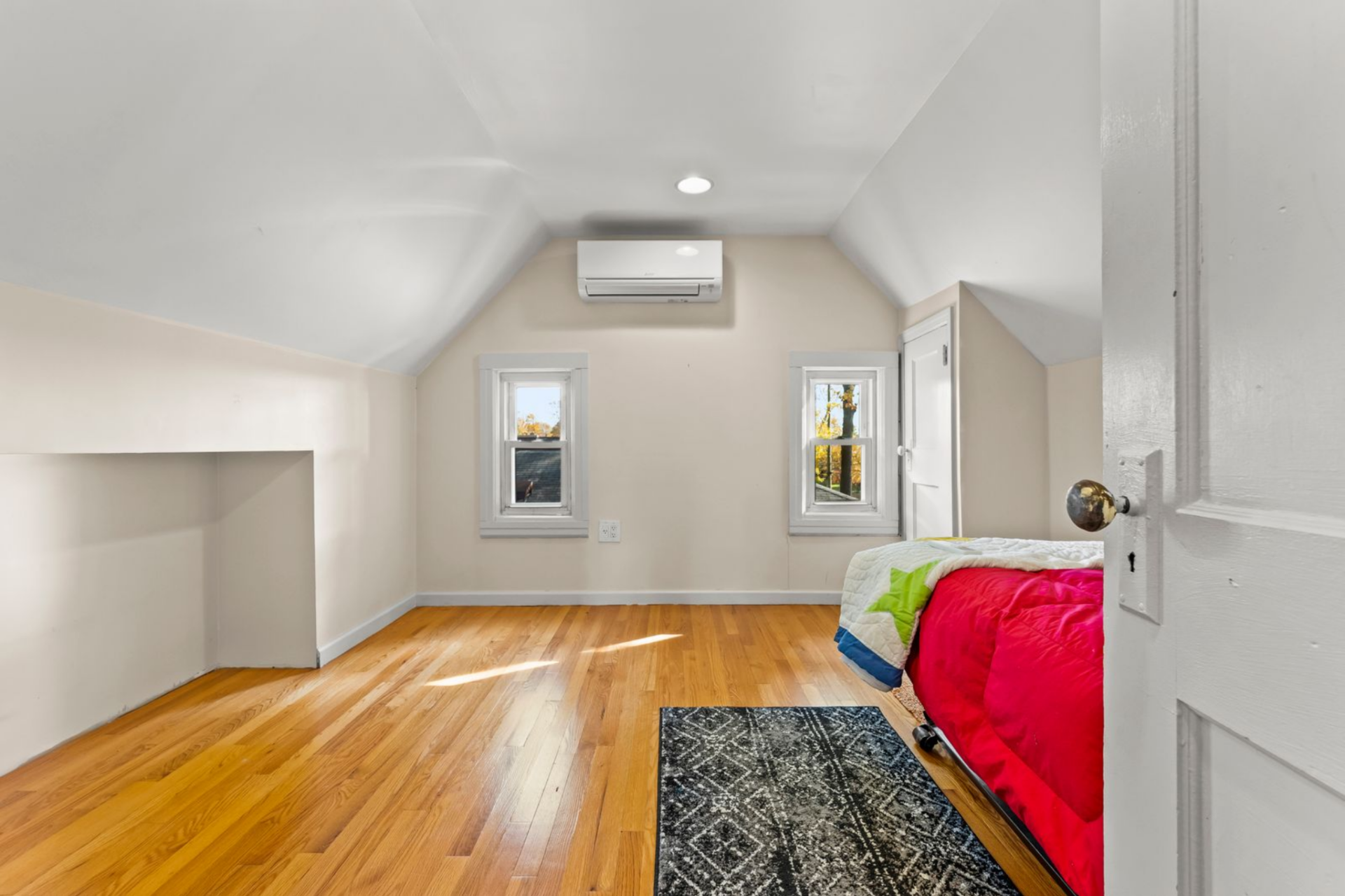 Two small windows are set into the far wall, bringing in light at a lower height, while the bed is positioned off to one side to keep the center of the room open.