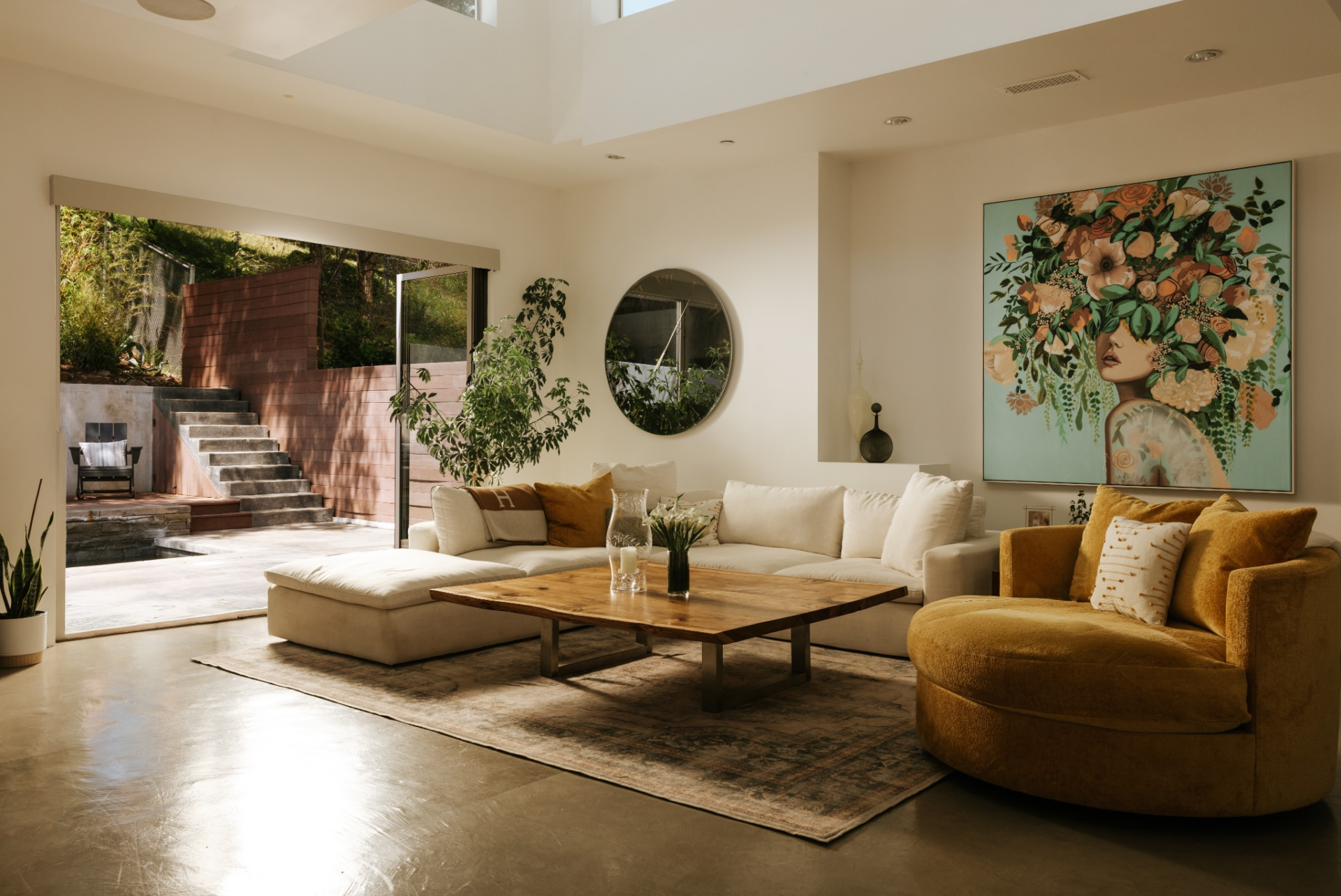 At the center, a low-profile sectional and lounge chair are arranged around a wood coffee table, grounding the space without blocking the flow of light.