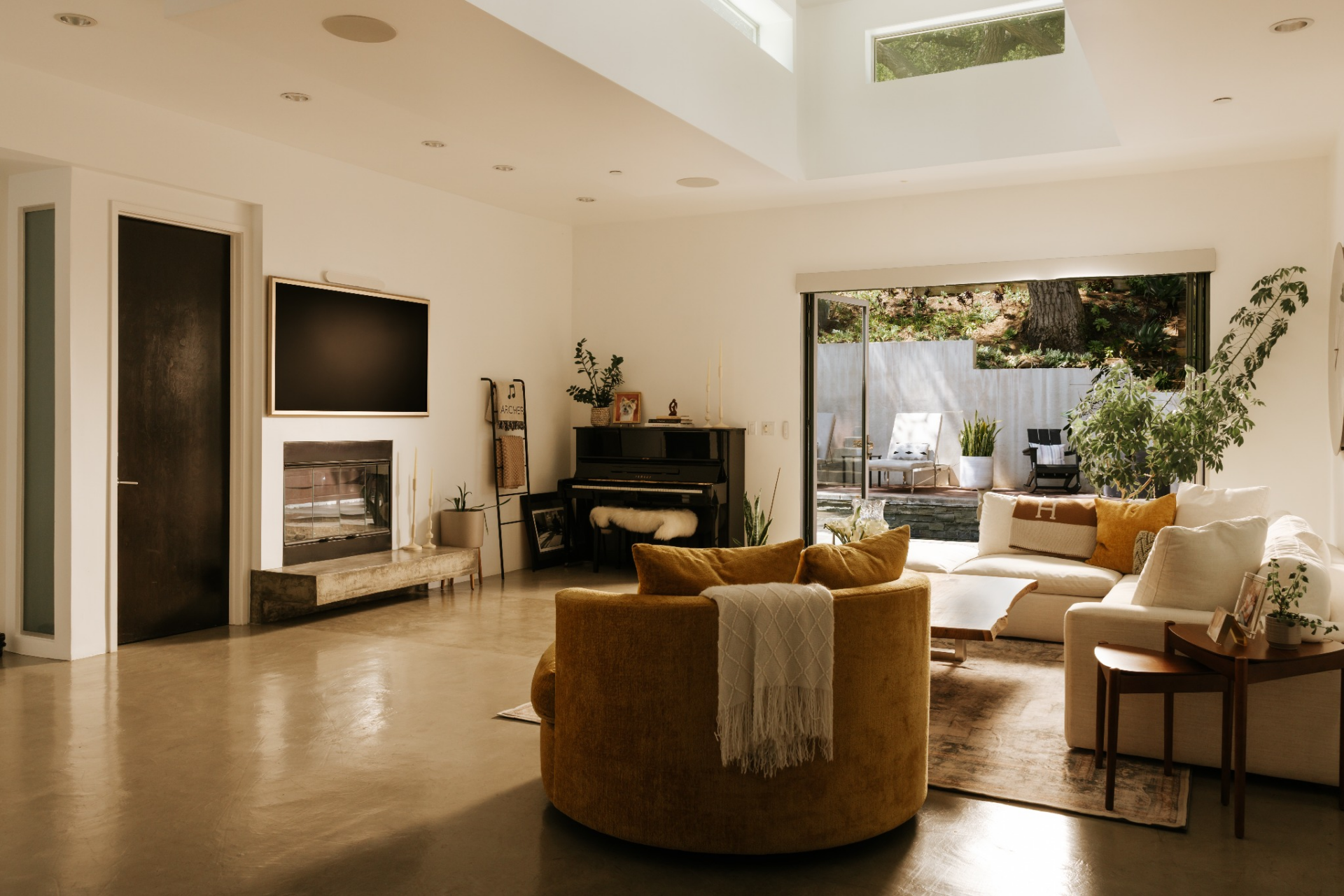 Along one wall, a fireplace and mounted screen are built into a clean, minimal surround, while a piano and additional seating sit just beyond.