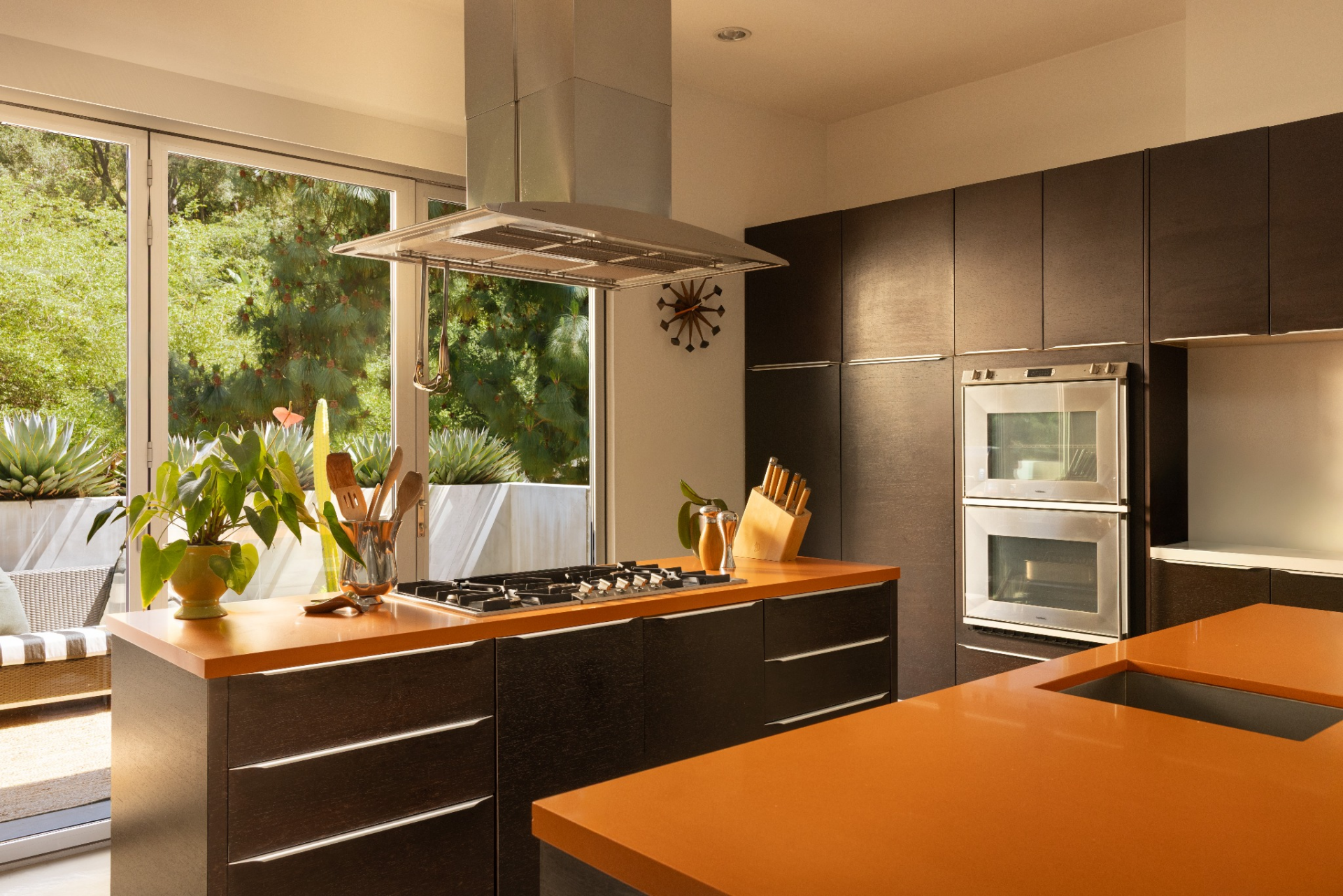 One island houses the cooktop beneath a suspended stainless steel hood, while the other provides additional prep space and an integrated sink, allowing the layout to function efficiently from either side.