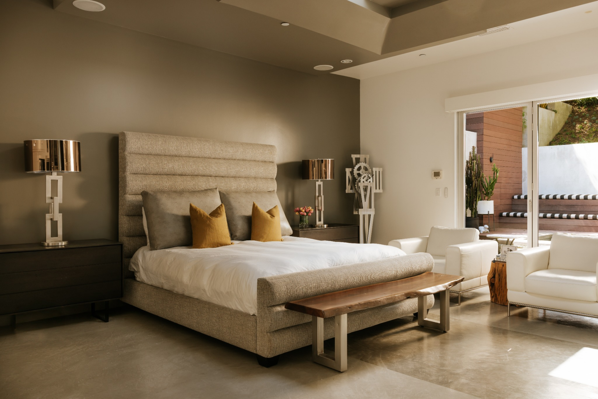 The bedroom centers on a large upholstered bed set against a dark accent wall, which gives that side of the room more definition while the rest of the space stays bright and minimal.