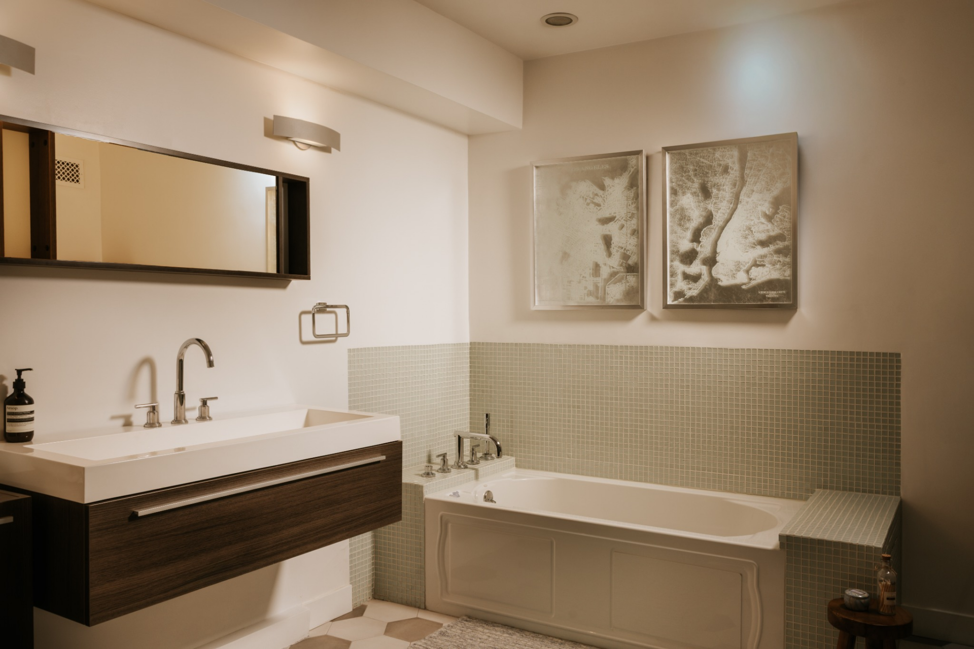 The bathroom features a floating vanity with a dark wood base that sits opposite a soaking tub wrapped in small light green square tile, with the tile continuing around the surround.