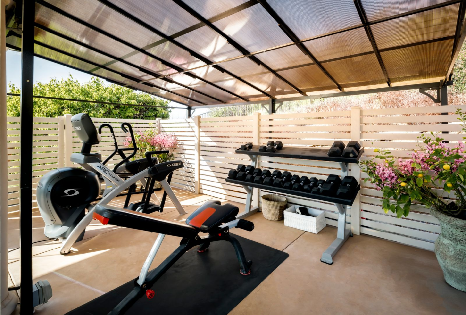 Tucked within the same glass-enclosed space is an outdoor fitness space. Covered for shade and privacy, it has cardio equipment and free weights, allowing for workouts in an open-air setting.