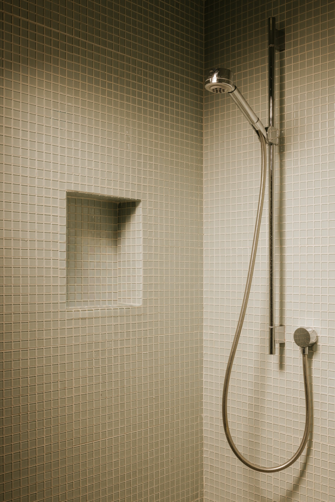 In the shower, the same mosaic lines the walls and around the built-in niche, keeping the bath consistent with the rest of the bathroom and giving the suite a clean, modern finish.