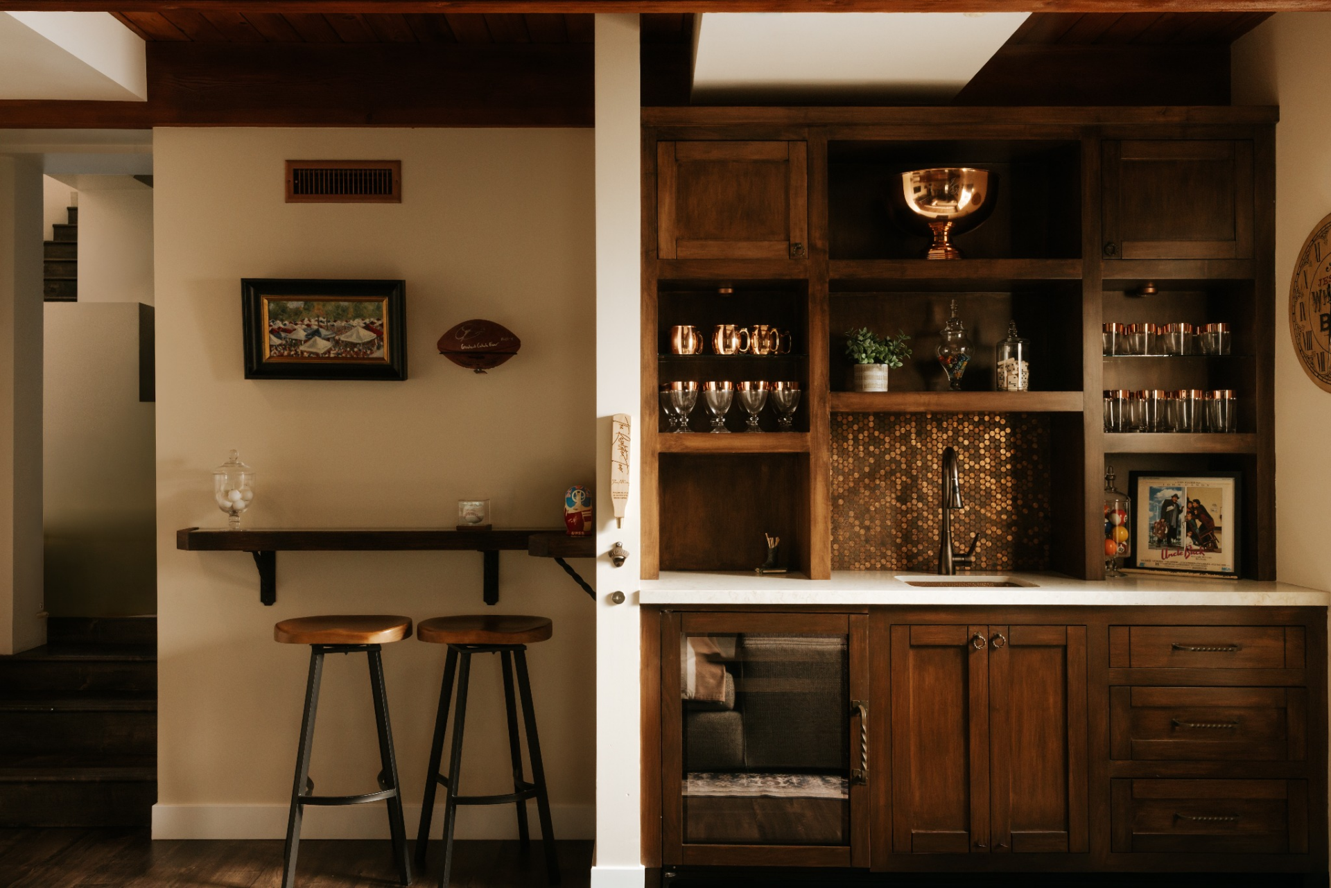 Open shelving, upper cabinets, undercounter refrigeration, and a sink turn it into a full-service station, while the warm backsplash adds a small point of contrast against the darker millwork.