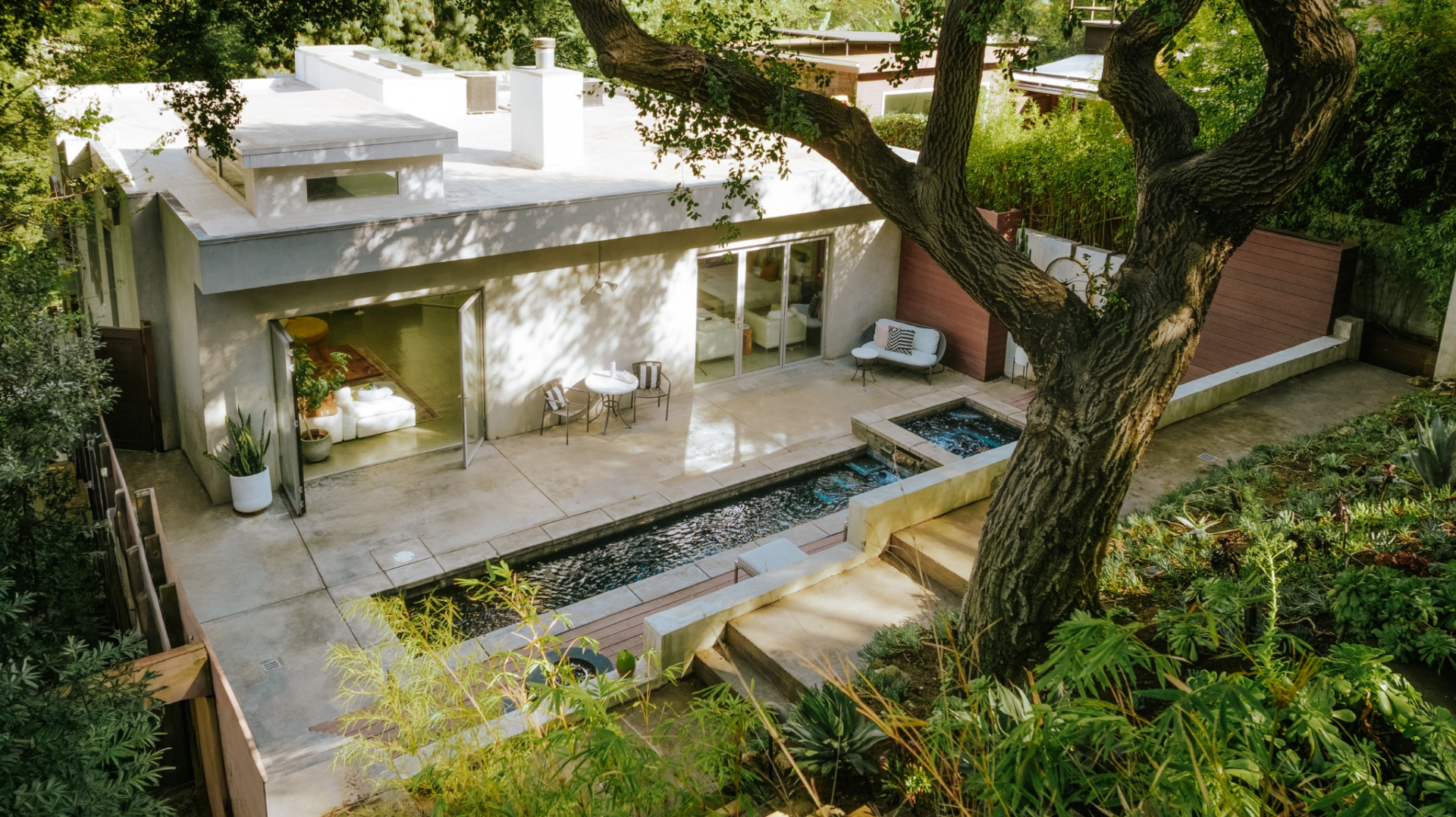 From the house, large openings lead directly onto a broad concrete terrace, where the water runs parallel to the hill behind it.