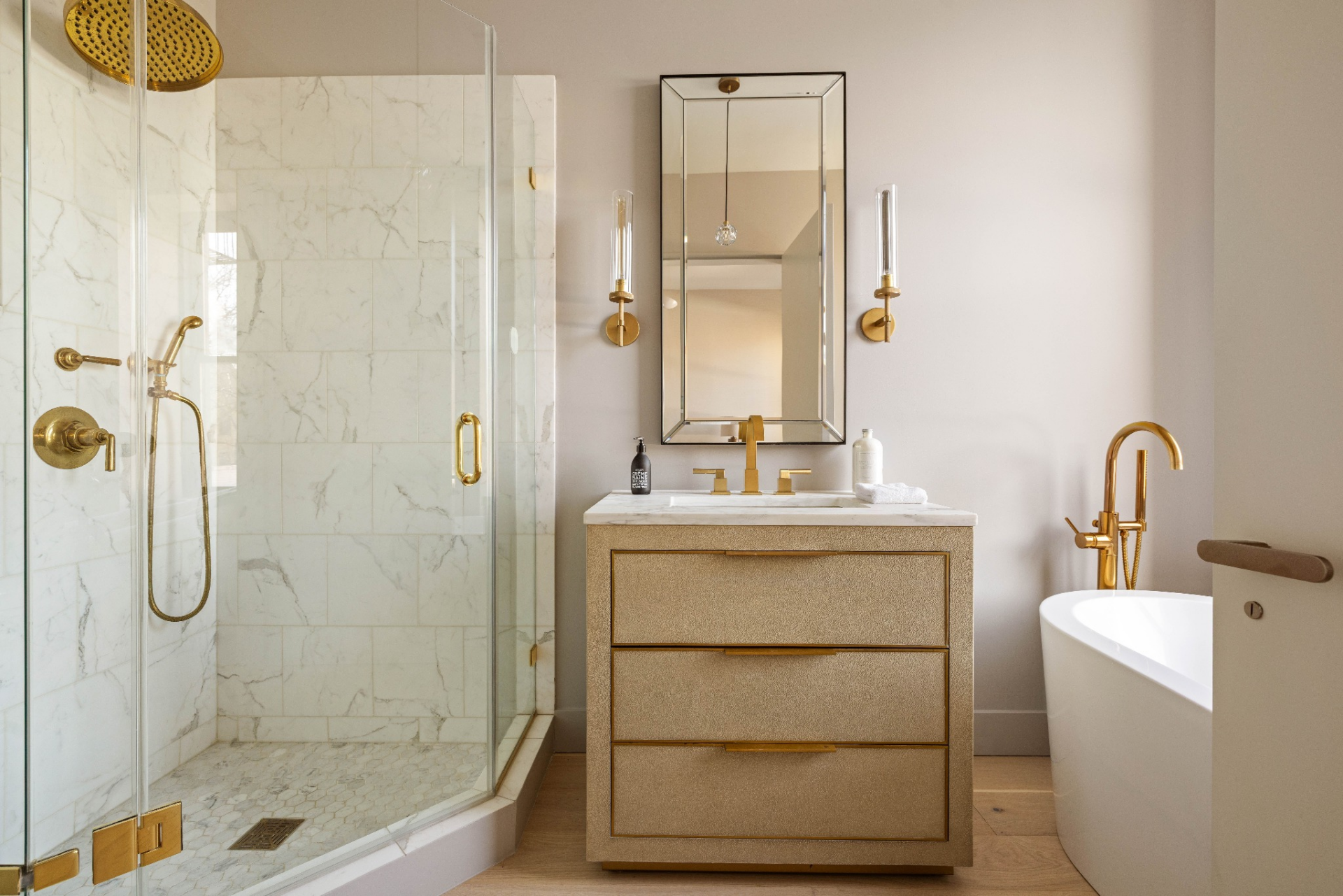 A compact vanity sits beneath a framed mirror with wall-mounted lighting, while the glass-enclosed shower runs along one side, and a freestanding tub on the other.