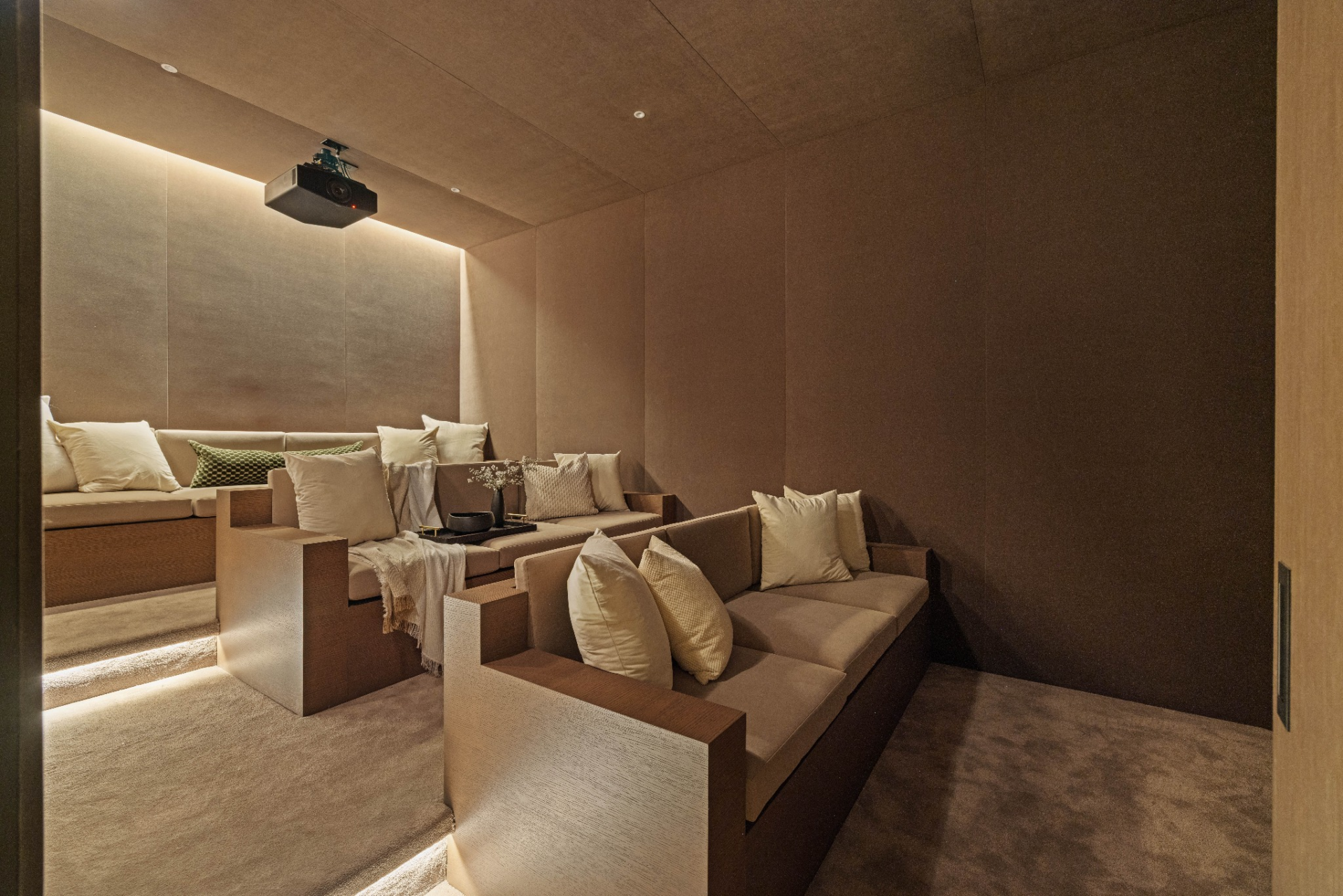 Soft strip lighting runs along the risers, while the walls and ceiling are wrapped in the same dark material palette, keeping the room visually quiet and focused around the projector setup.