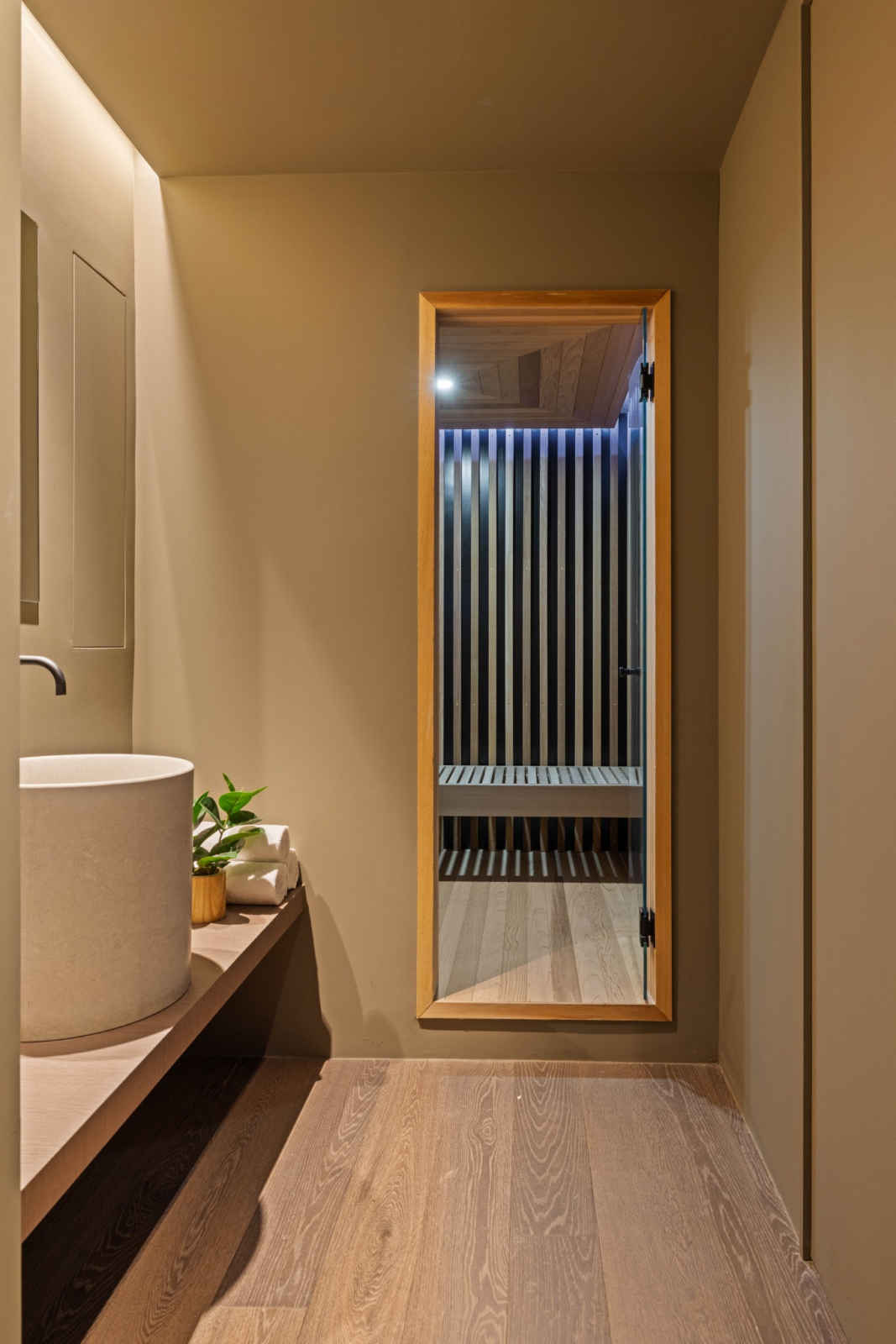 Off the basement's bathroom, the sauna is set behind a full-height glass door, framed in natural wood.