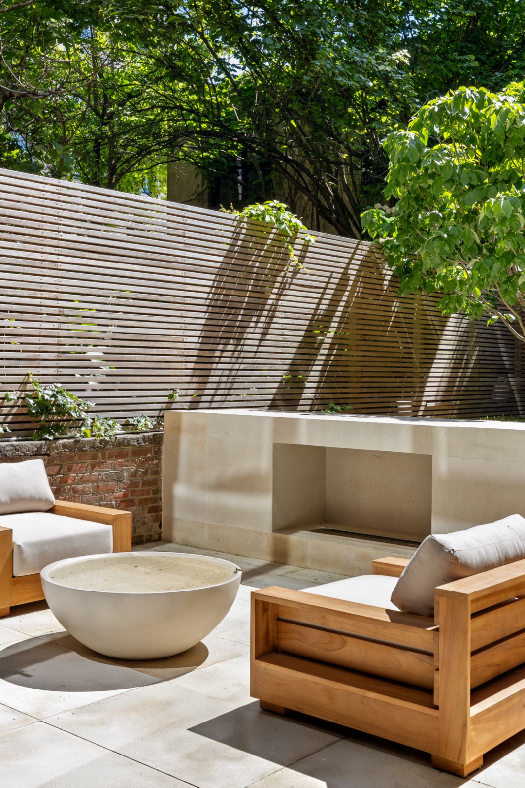 Extending directly off the garden level, a paved terrace sits just outside, arranged as a compact lounge with low wood-framed seating, pale cushions, and a round concrete-style table at the center.