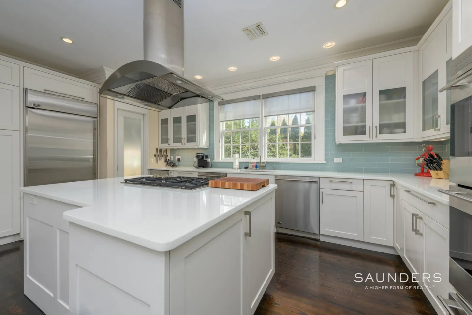 From the dining room, the layout moves into a bright kitchen organized around a central island with a built-in cooktop and a large stainless hood suspended above it. 