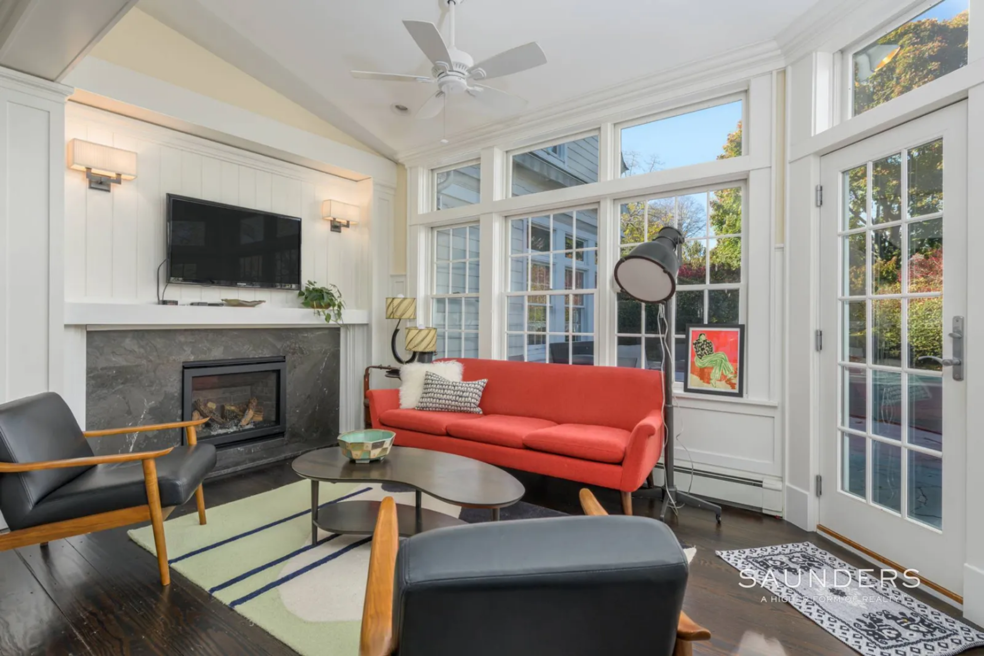 The layout centers on another, more modern, fireplace with a simple white mantel and darker stone surround, with seating arranged closely around it, including a sofa, lounge chairs, and a low coffee table.