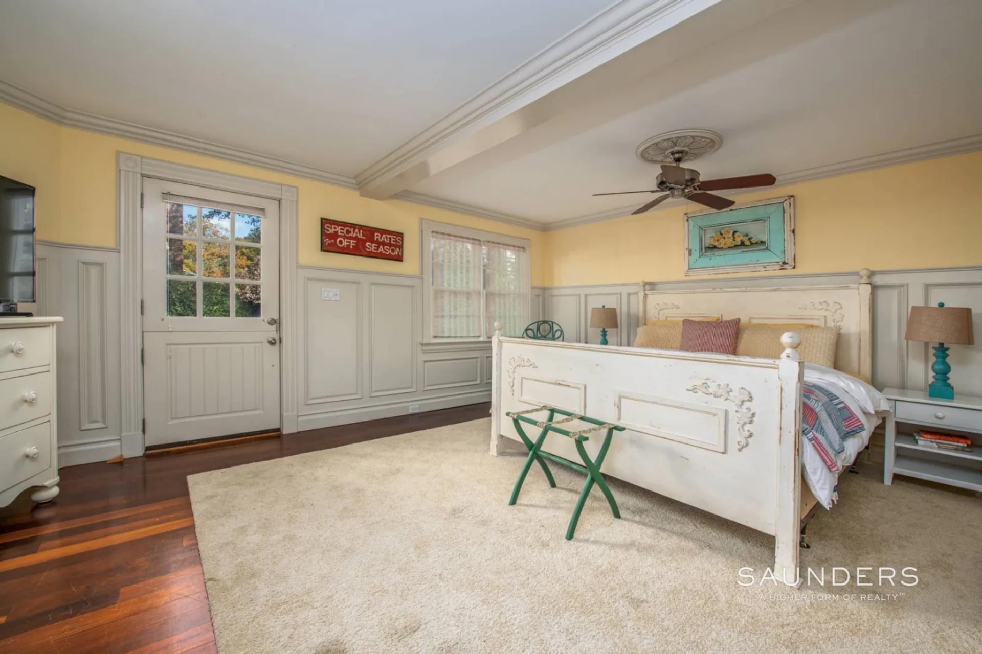 The bedroom takes on a softer, more casual tone with pale yellow walls, wainscoting, and an antique-style bed frame. 
