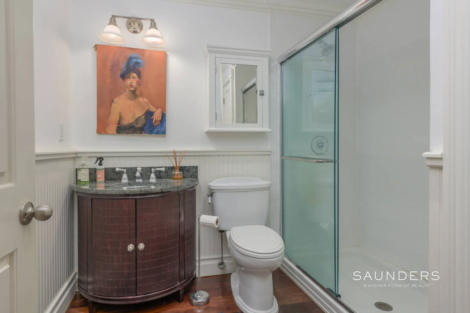 The bathroom is compact and straightforward, with a glass-enclosed shower running along one side and a curved dark wood vanity placed opposite it. 