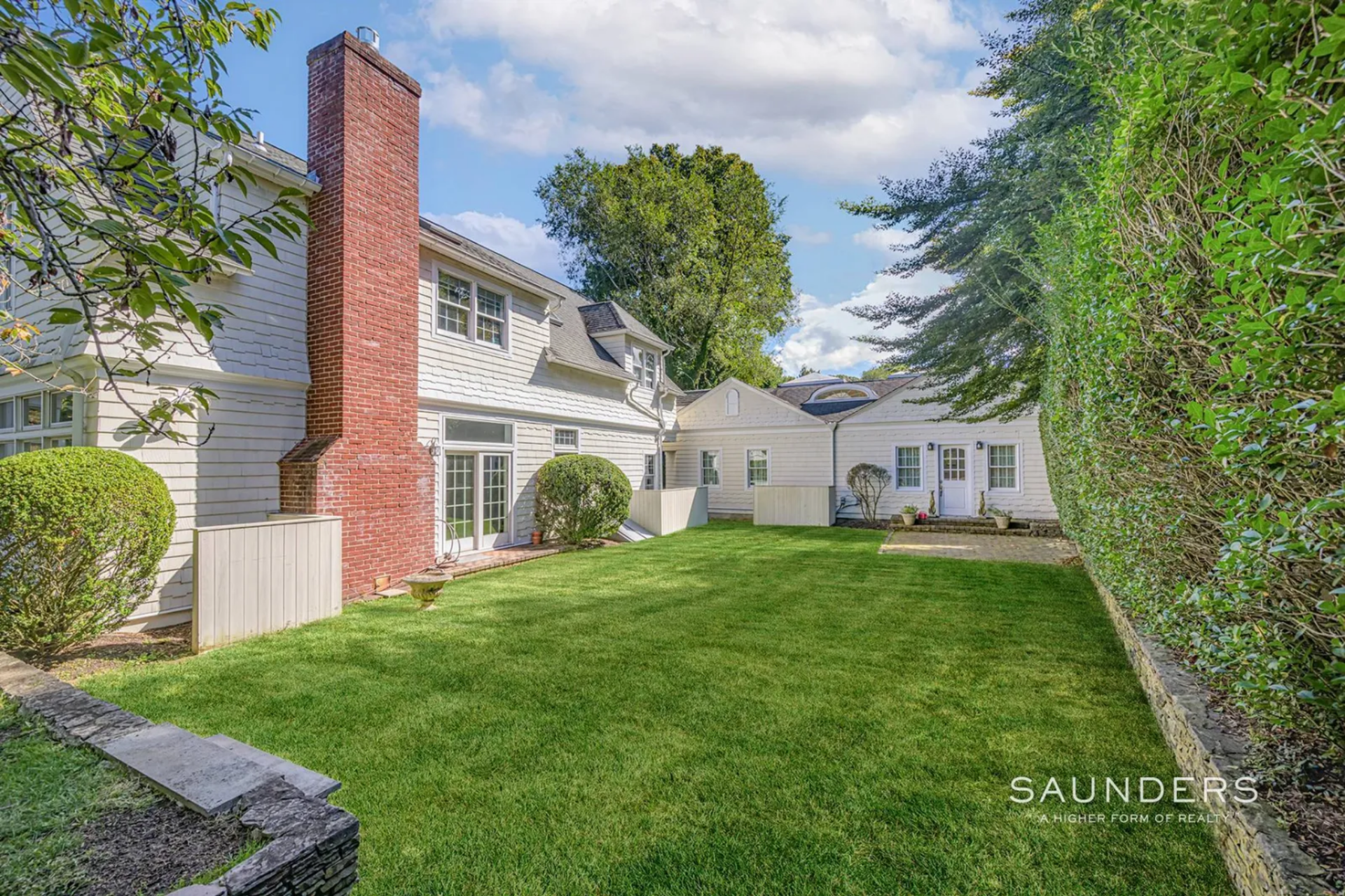 Stepping outside, the first area opens into a broad stretch of lawn positioned between the main house and the detached cottage, creating a central outdoor corridor that connects the two structures.