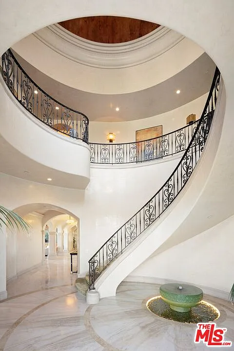 The mansion opens with a domed foyer where a sweeping staircase curves beneath the circular ceiling, while a stone fountain set into the floor adds another formal focal point at the entrance.