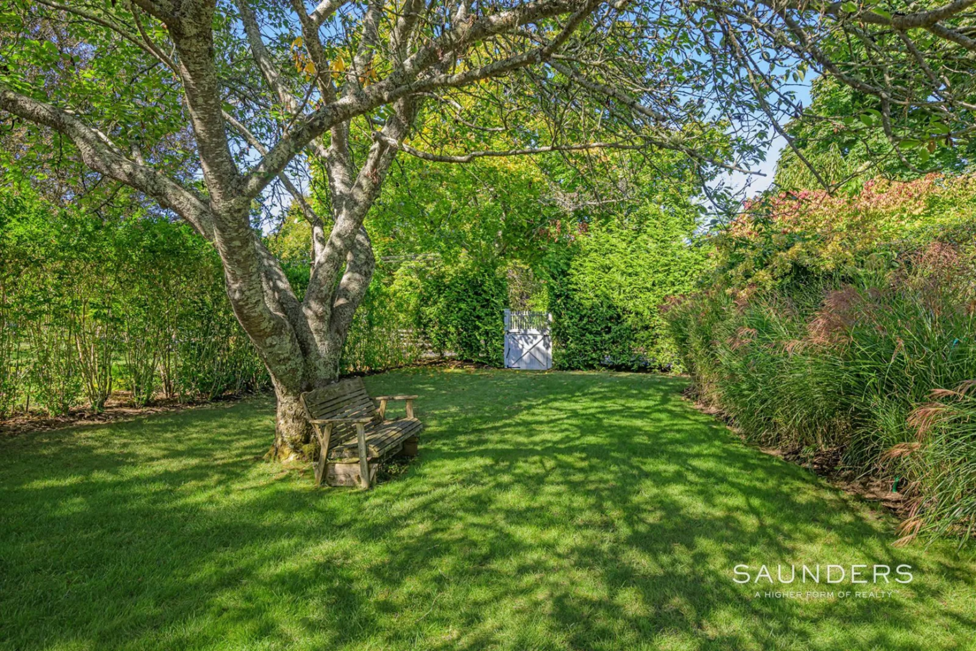 Toward the far end, the landscaping becomes more enclosed, with taller plants and a shaded sitting area beneath a tree.