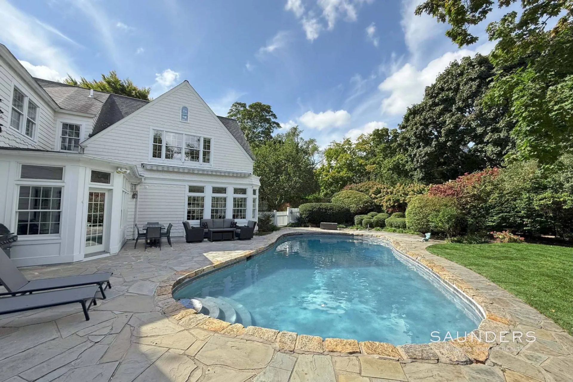 Around the corner, the layout transitions into the pool area, where a freeform heated gunite pool is set into a bluestone patio that wraps around its perimeter. 