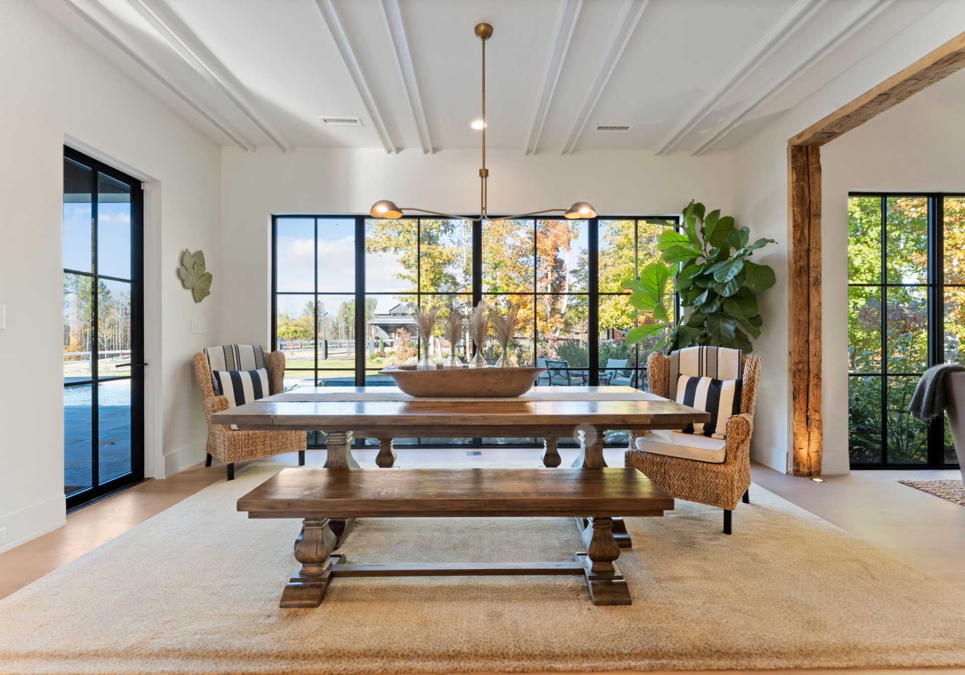 Through the side doorway, the dining area features a long wood table with matching bench seating and woven host chairs that add texture and soften the room’s crisp lines.