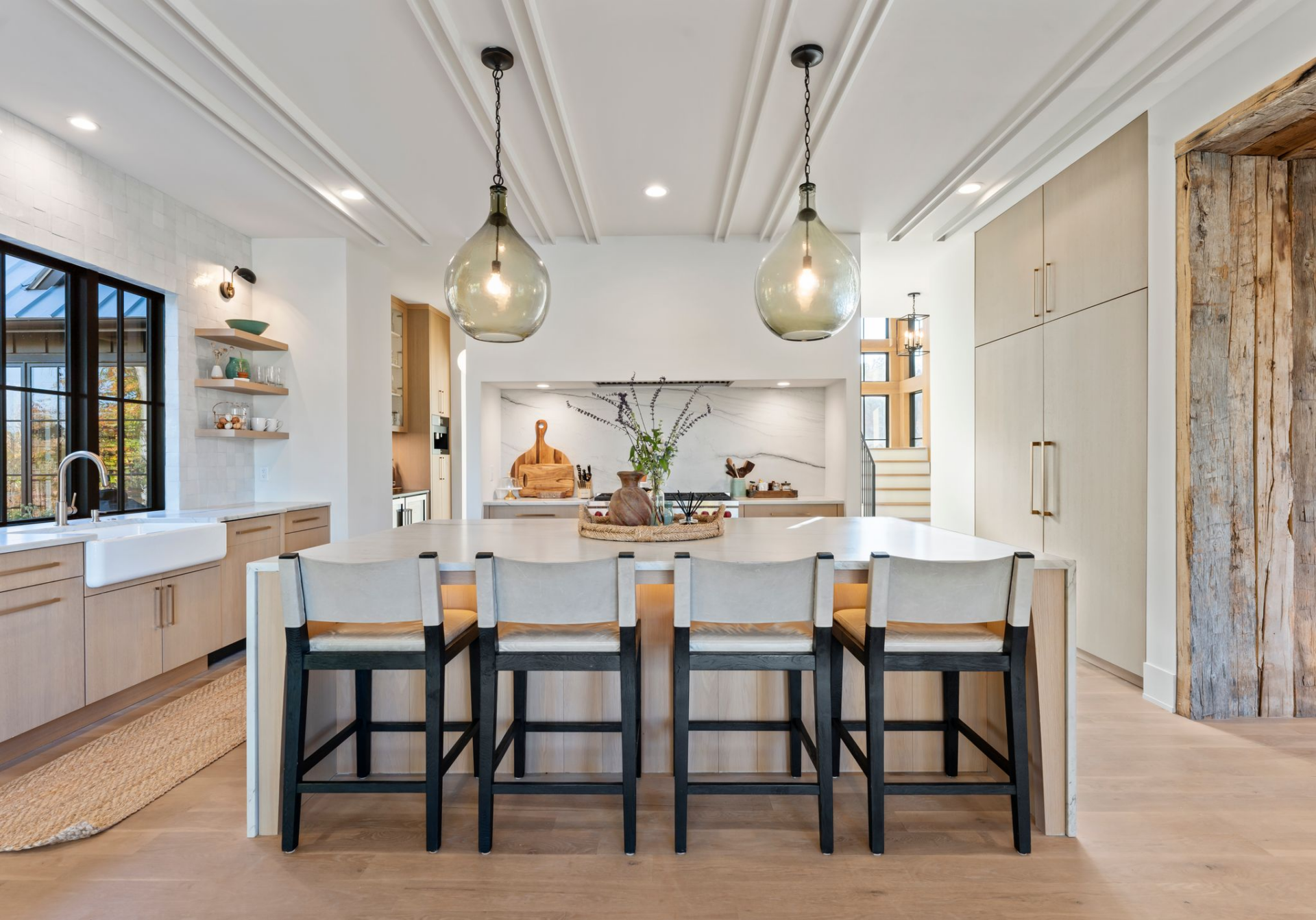 Across from the dining area, the bright kitchen opens up around a large waterfall-edge island lined with bar seating beneath two pendant lights, and detailed ceiling trim that helps define the space without closing it off from the dining area.