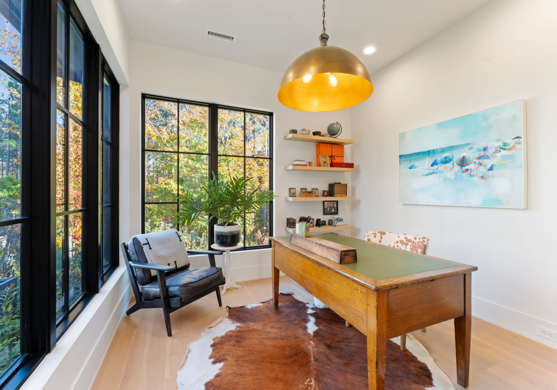 Off the main living spaces, the home office is set up as a compact workspace with an antique wood desk paired with a leather chair, a patterned side chair, and a cowhide rug that adds another rustic touch. 