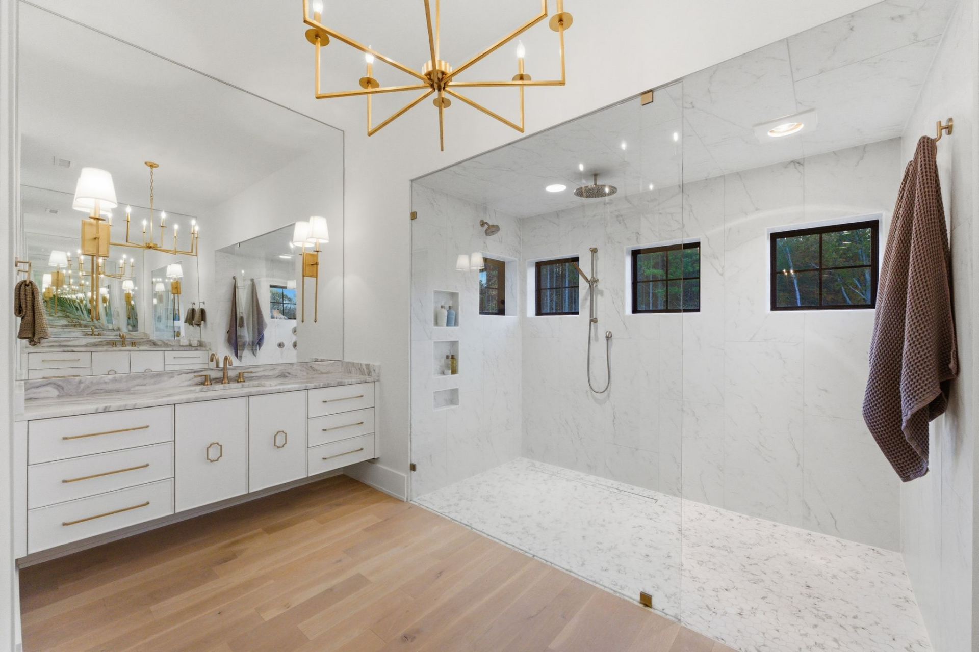 Brass hardware and a geometric chandelier add contrast, while small windows within the shower wall bring in natural light without compromising privacy.