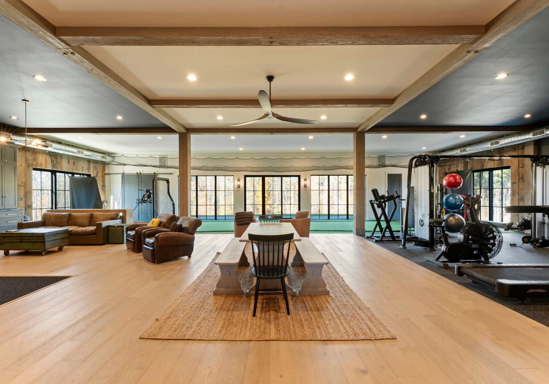 The structure opens into a wide, beam-lined interior that combines a sitting area, dining table, and full gym within one continuous space.