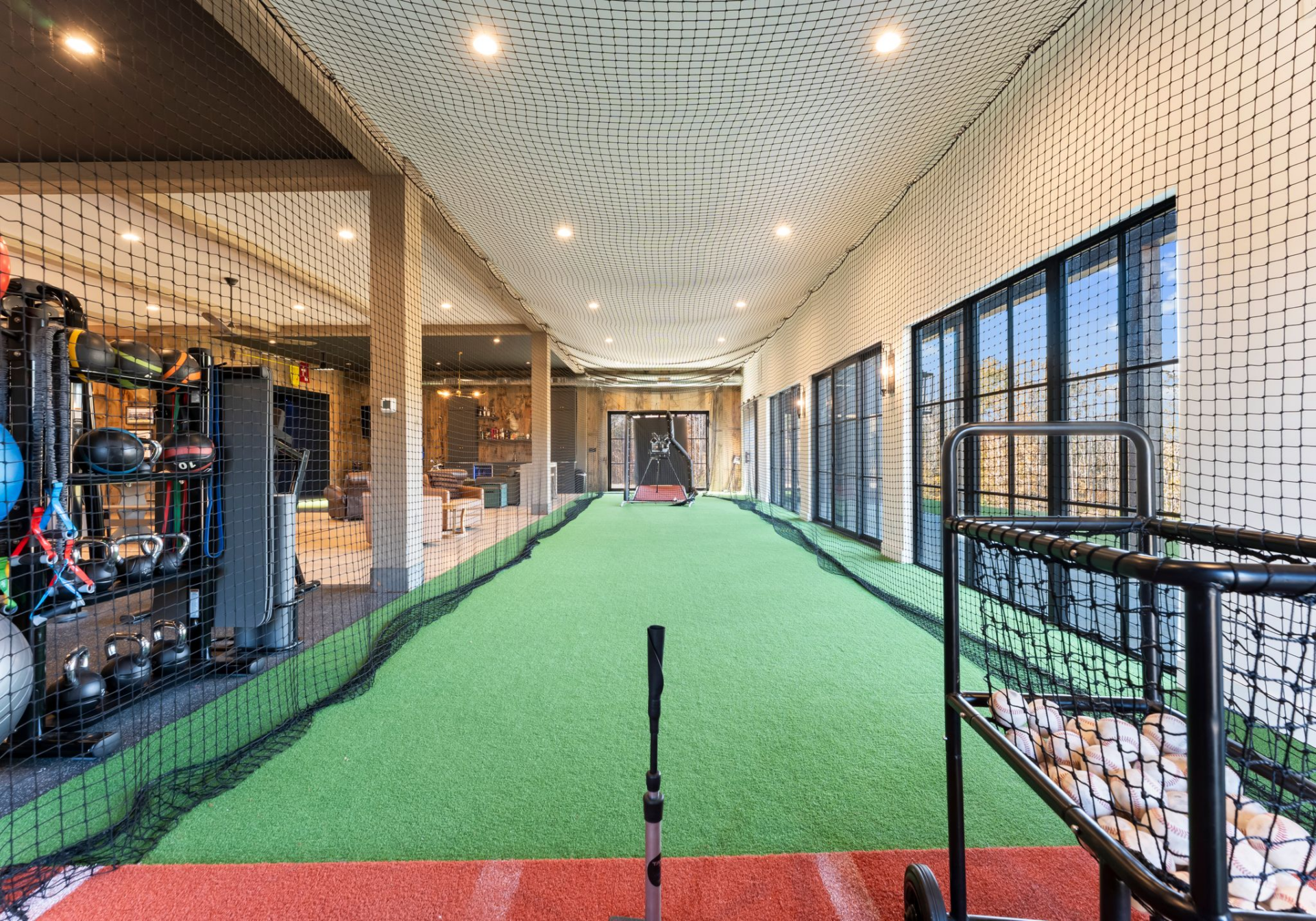 Running along the back of the structure, a fully enclosed batting cage stretches the length of the space, fitted with turf flooring and overhead netting.