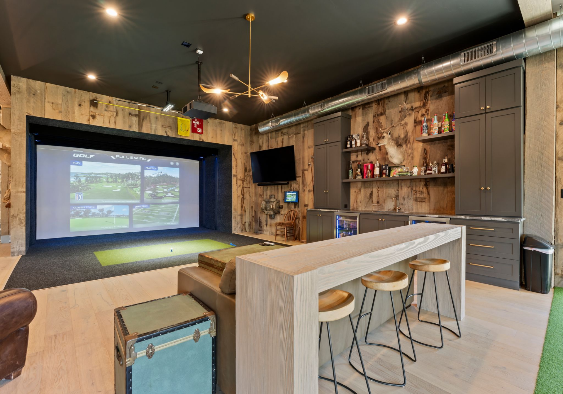A full golf simulator with a projection screen and hitting platform next to a built-in bar.