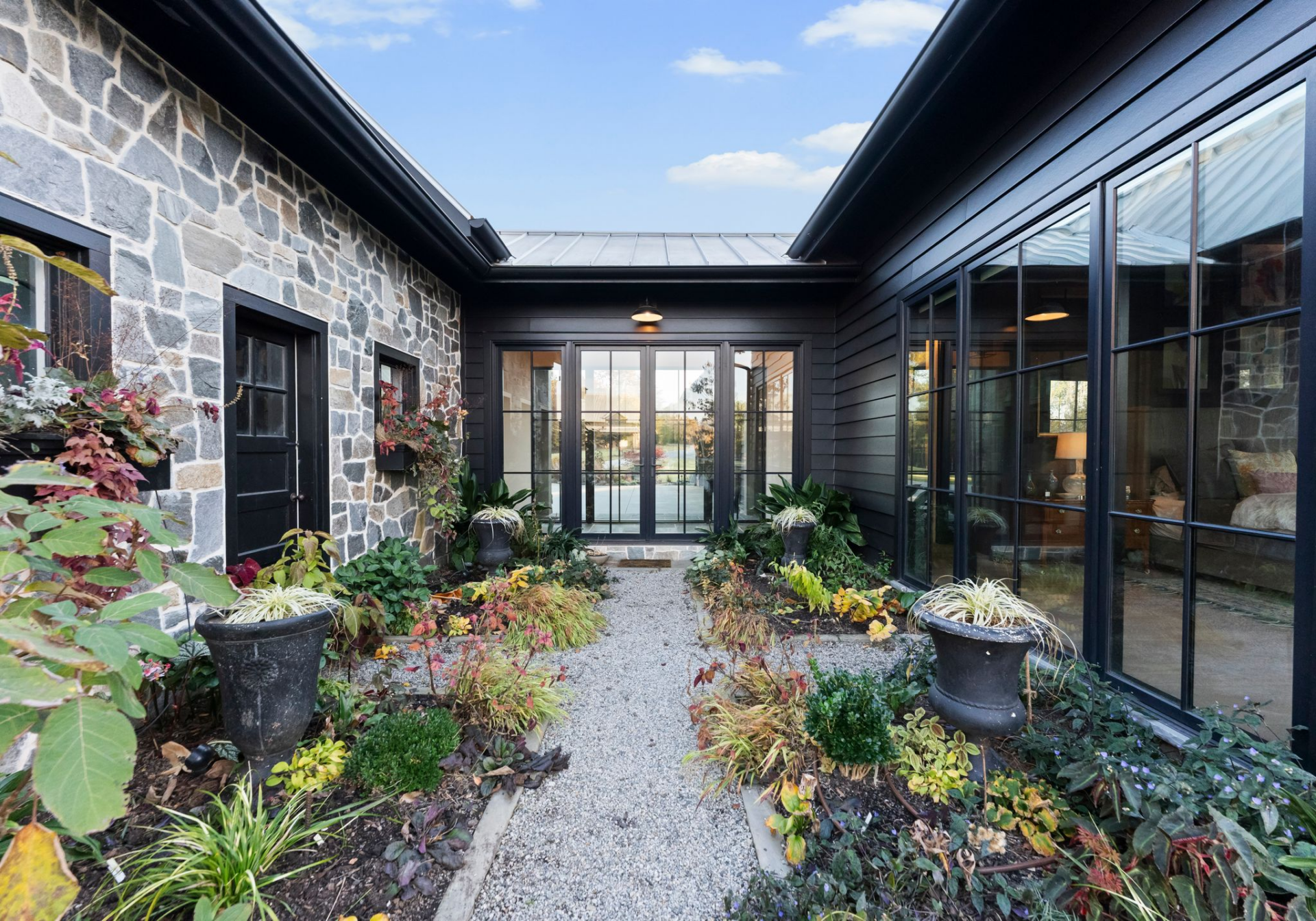 Positioned between two wings of the home, the garden courtyard acts as a central outdoor passage, lined with stone walls, black-framed windows, and a gravel walkway. 
