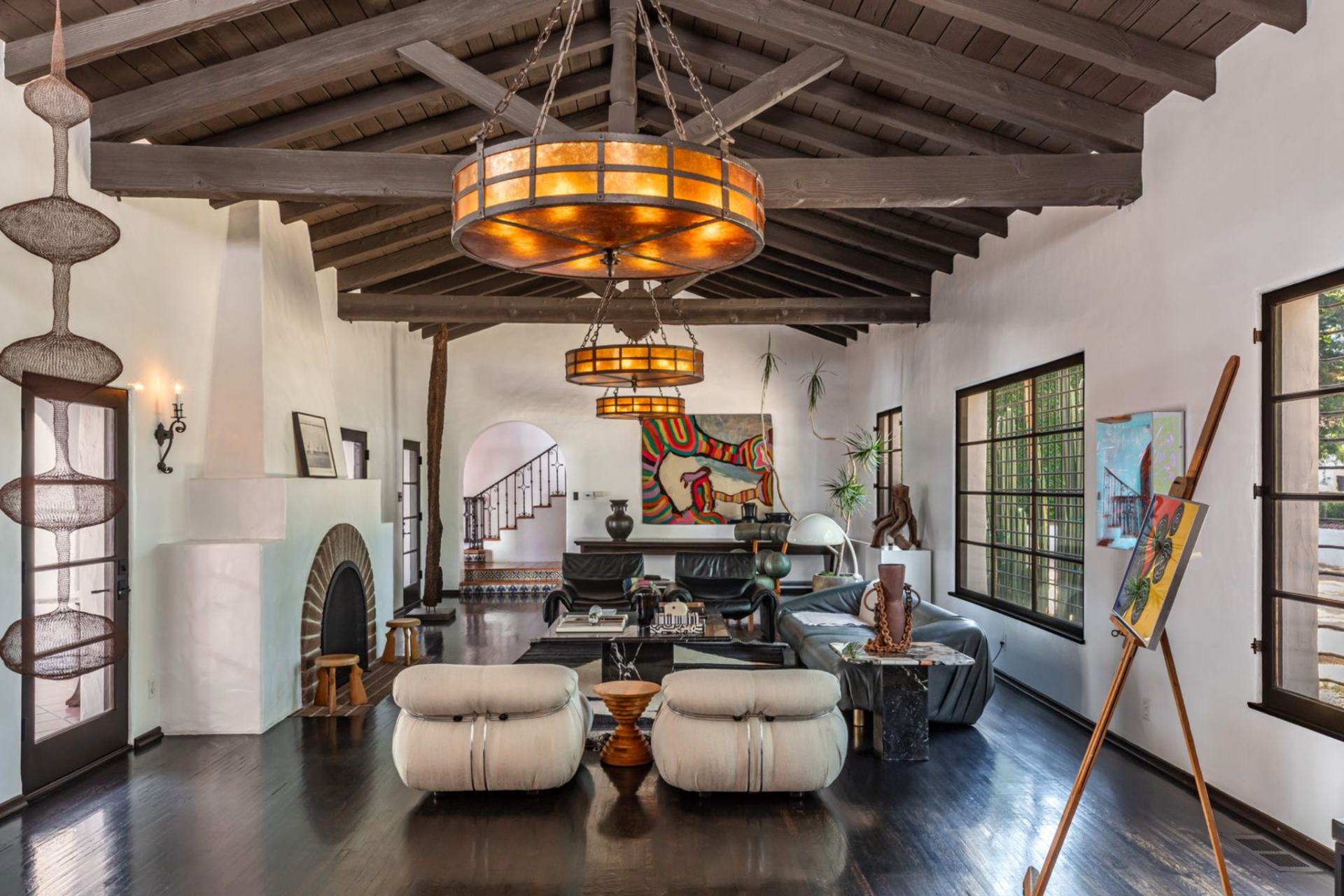 Below, the room is arranged around a plaster fireplace with a rounded brick surround, set against white walls that contrast with the dark-stained floors. 