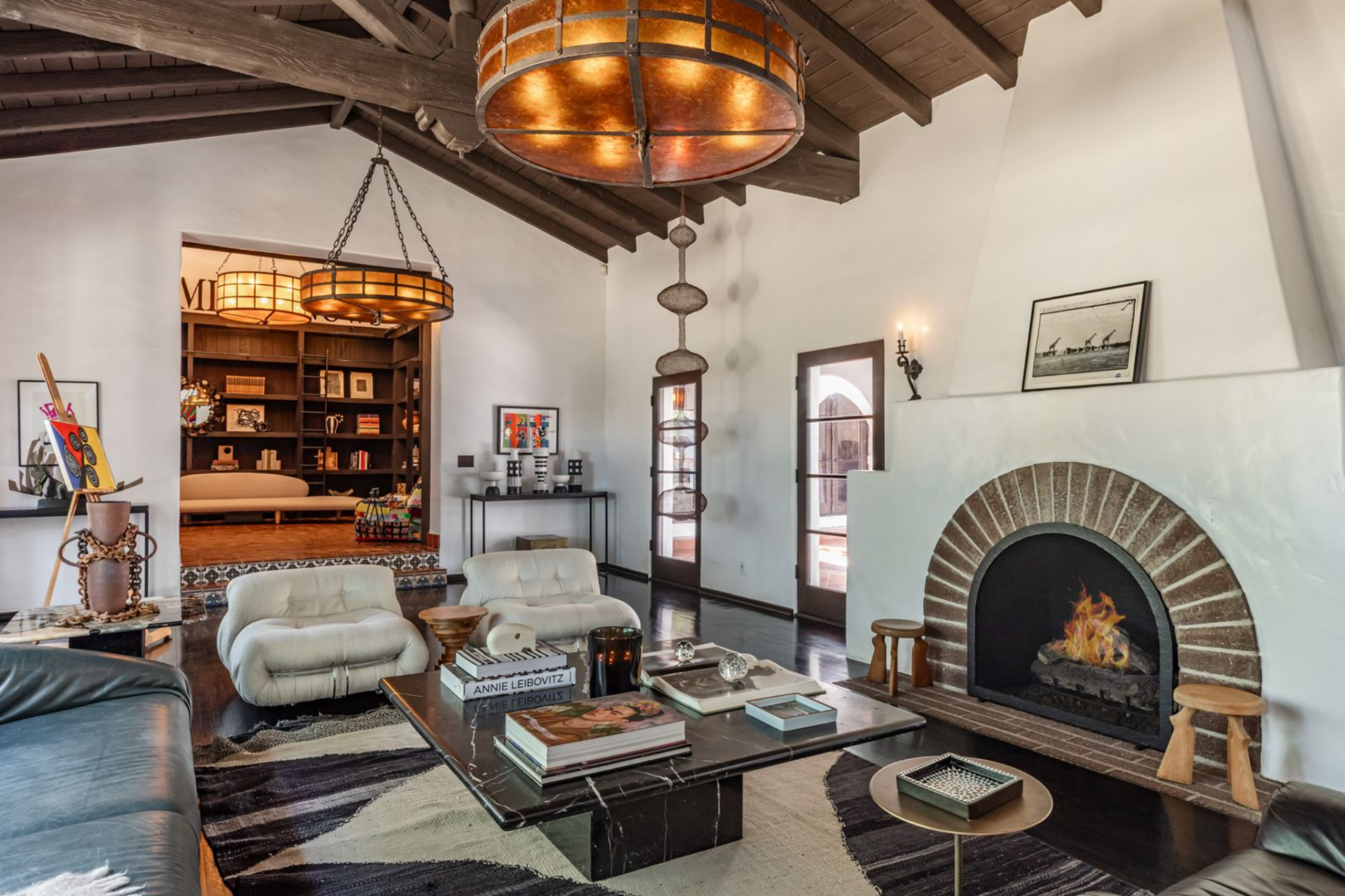 Dark wood beams stretch across the pitched ceiling, drawing the eye upward while a series of oversized, amber-toned chandeliers hang low over the space.