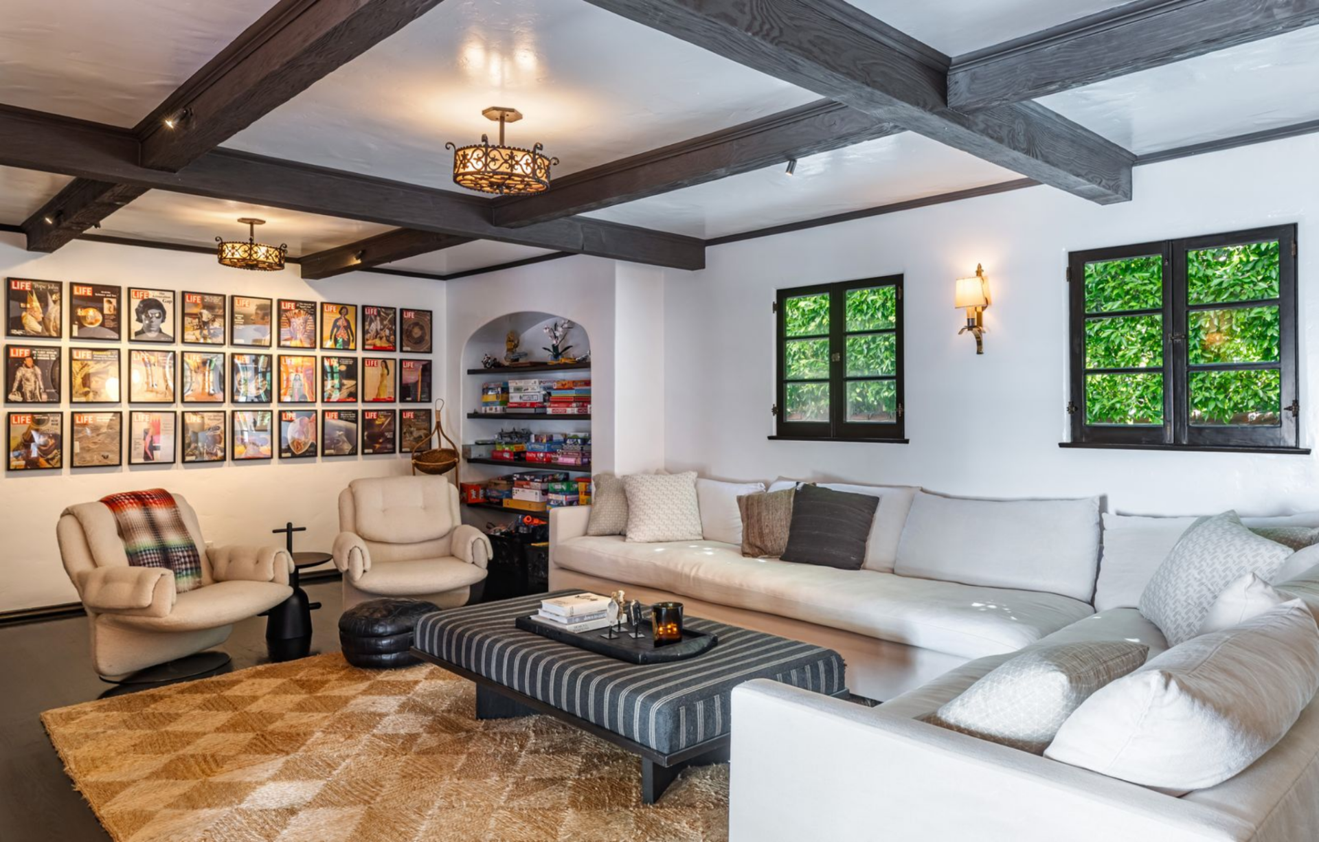 One side is arranged as a lounge, with a large sectional, a low ottoman, and two club chairs set beside a wall of framed LIFE magazine covers and an arched built-in bookshelf filled with games.