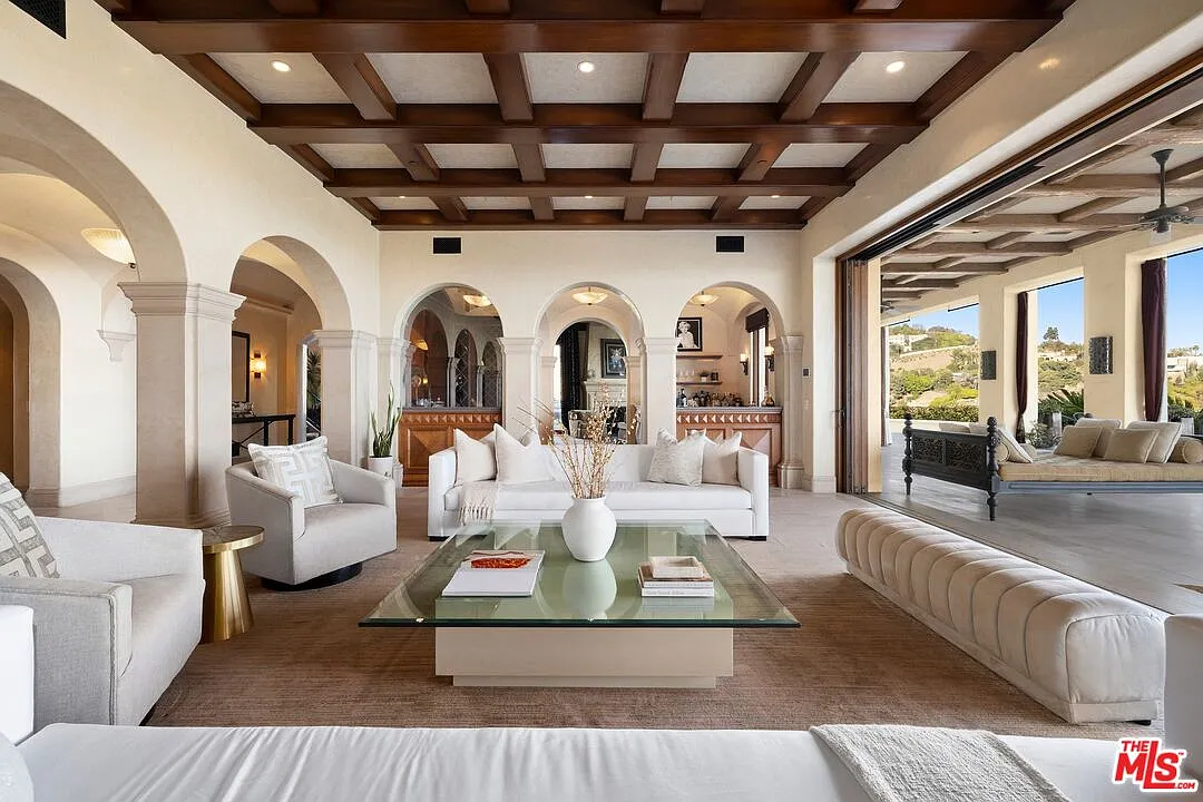 A dark coffered ceiling gives the room weight overhead, while a series of arches along the back wall frame a bar with built-in millwork, adding depth behind the main seating area.
